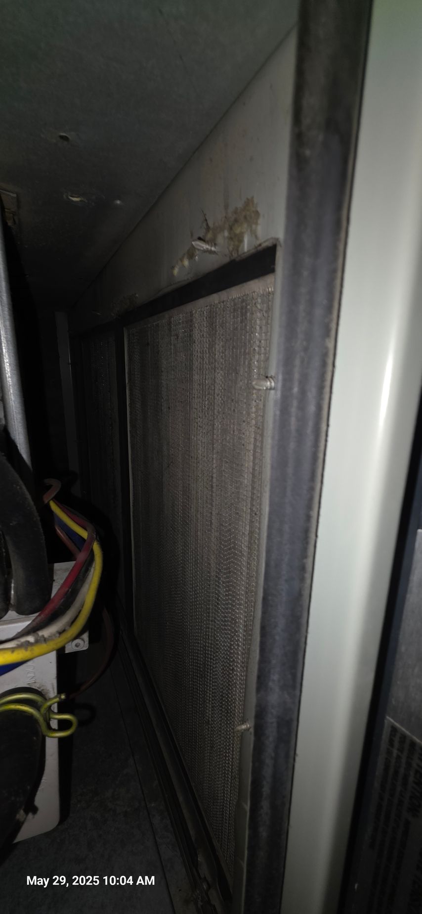A dirty air filter in an enclosed space with wires visible on the left side, light and dark tones.