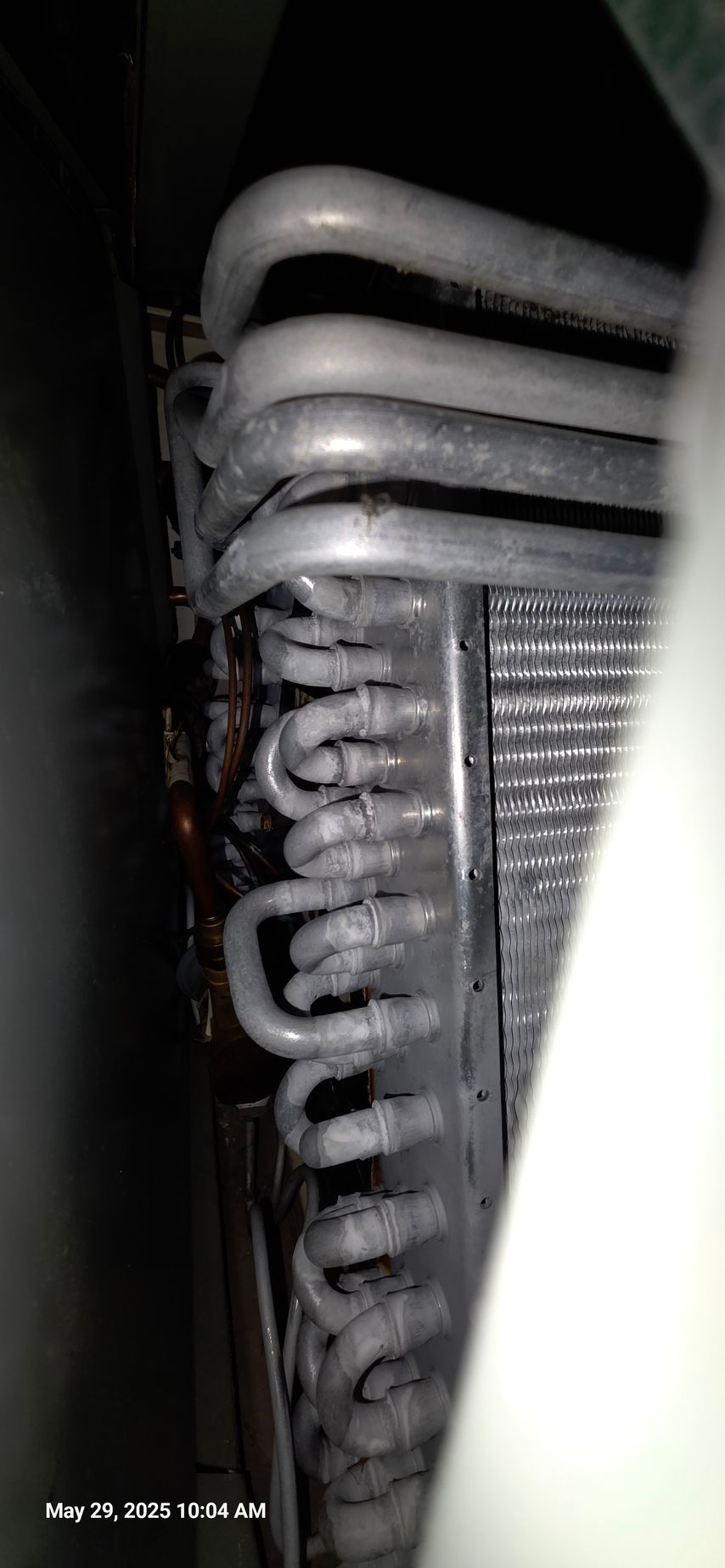 Close-up of a dusty air conditioning evaporator coil with curved metal tubes and fins.