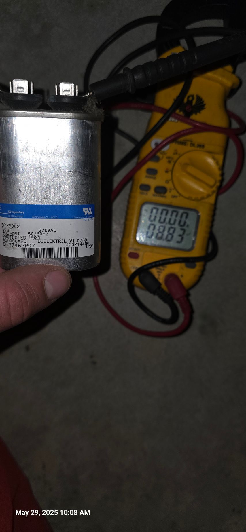 A cylindrical capacitor is tested with a multimeter, showing readings on the display.