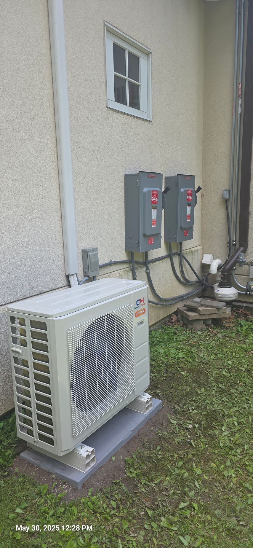 Air conditioning unit outside a building with electrical boxes and a small window.