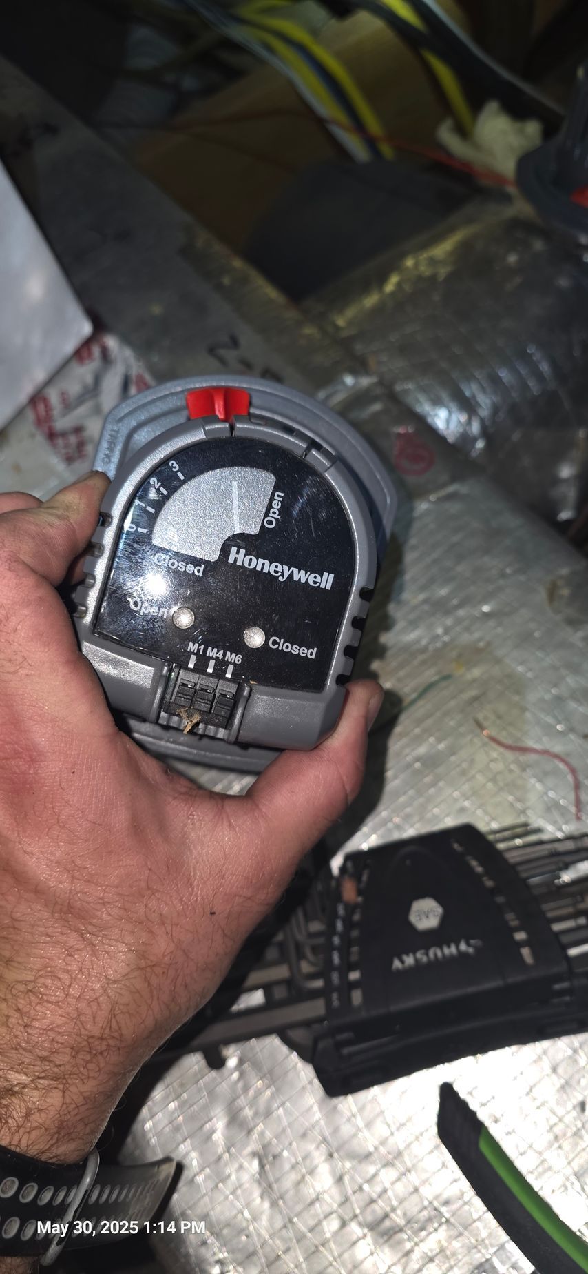 Hand holding a Honeywell pressure switch inside an HVAC duct. The switch dial shows pressure levels with a red indicator.