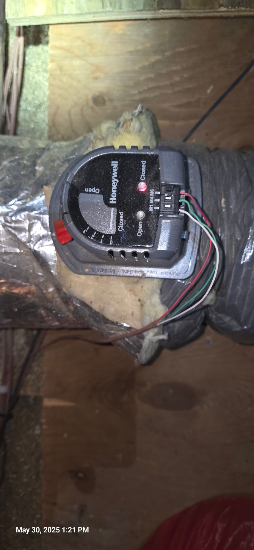 Honeywell damper control on ductwork, wired, in an attic or crawlspace. Red, green, white wires visible.
