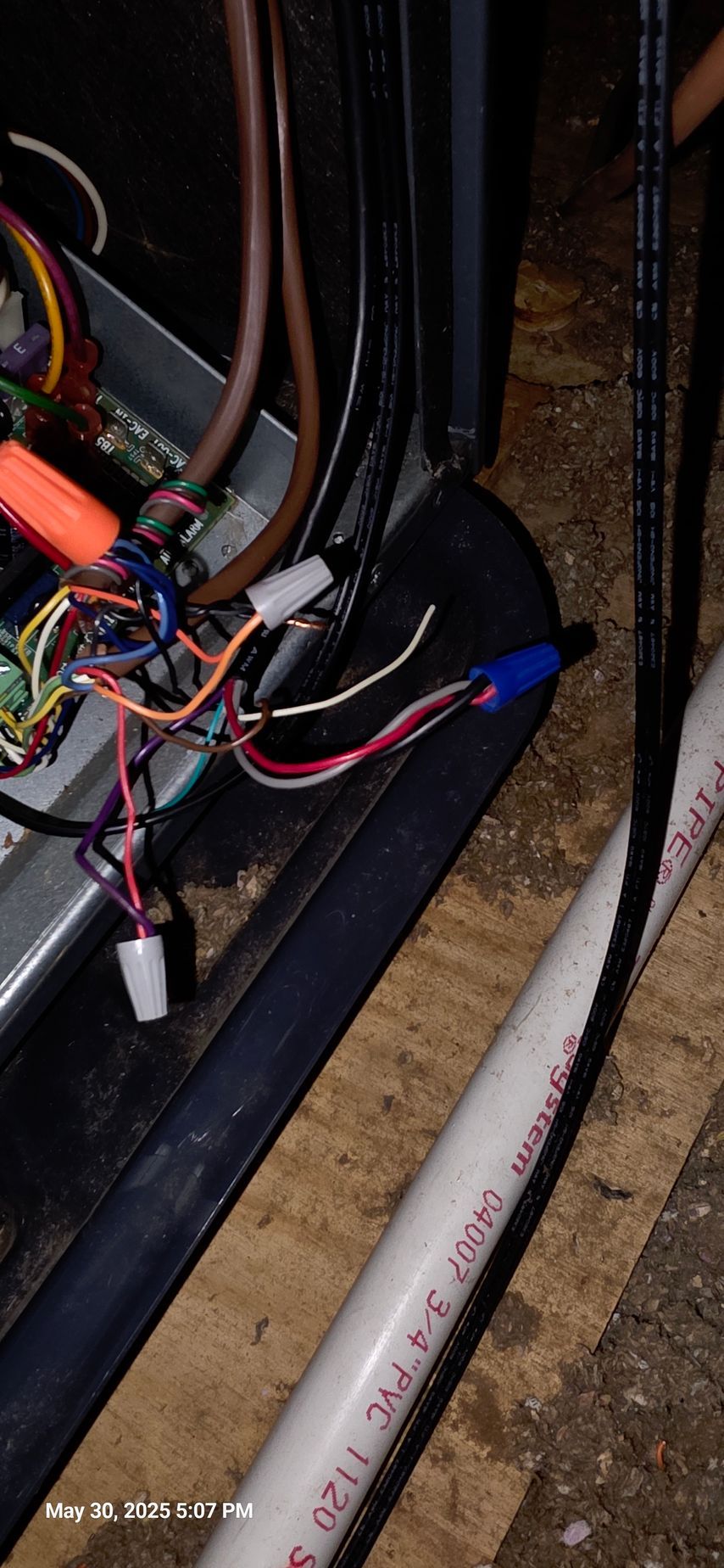 Wiring and connectors in a dark enclosed space, near a white PVC pipe.