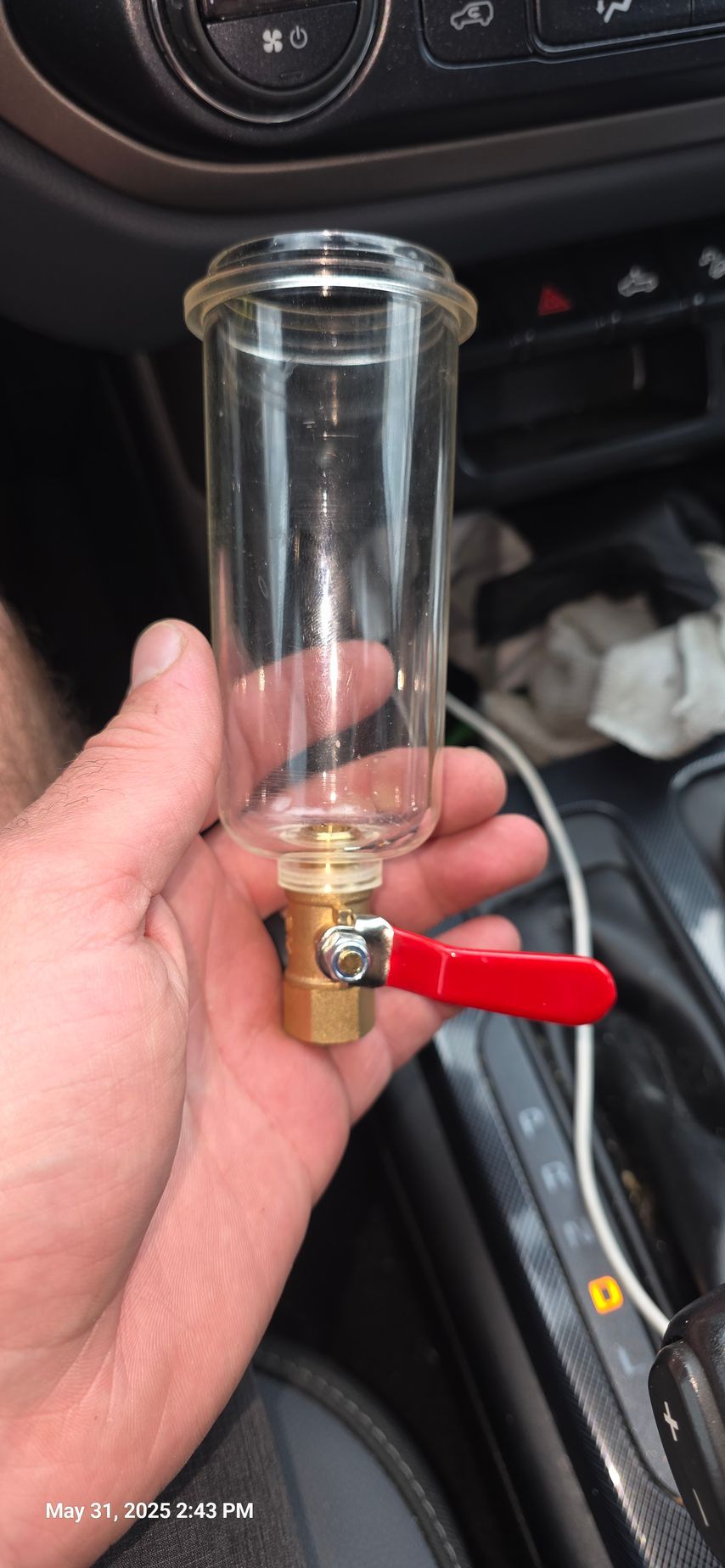 A person holds a clear glass tube with a red-handled valve in a car interior.