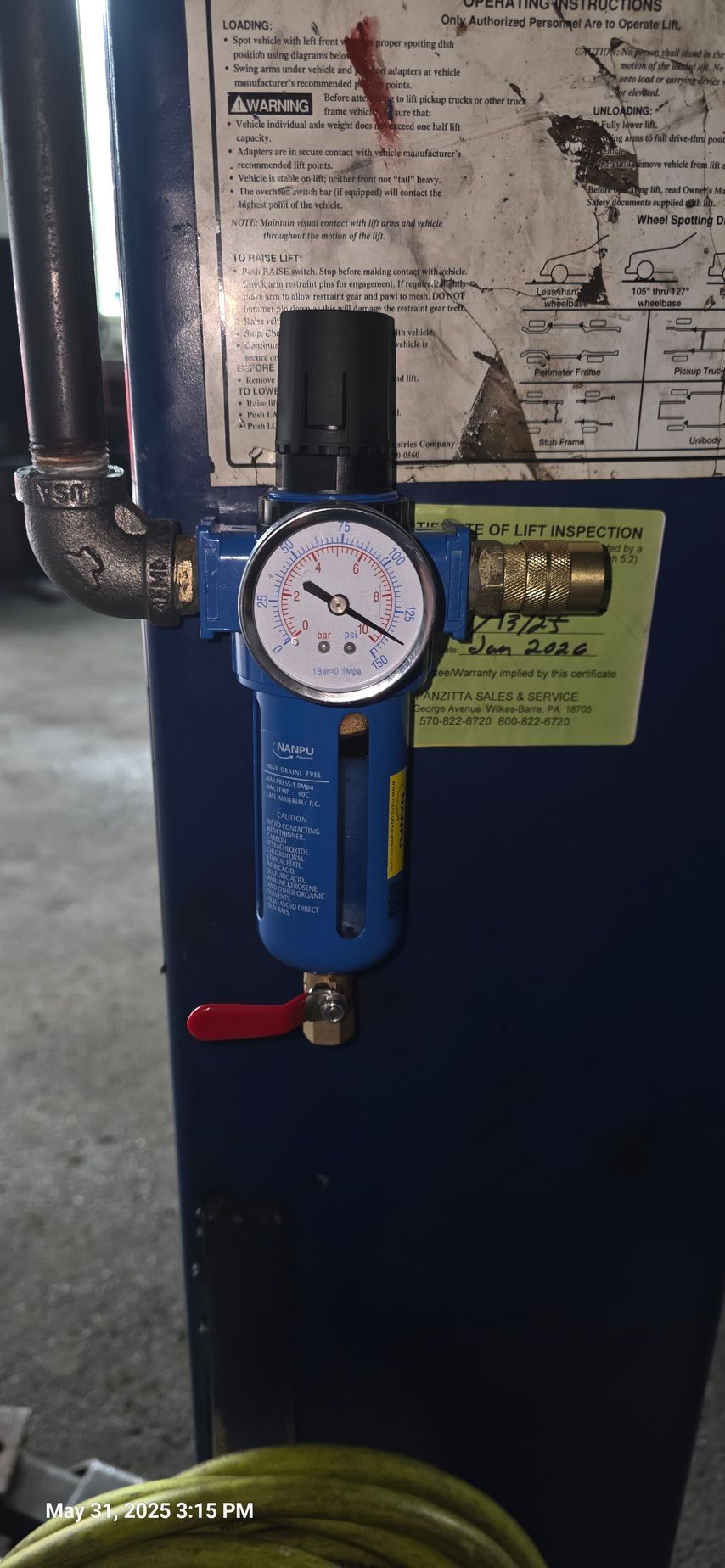 Blue air filter with pressure gauge and red valve on blue metal. Mounted on a large blue structure, with piping.
