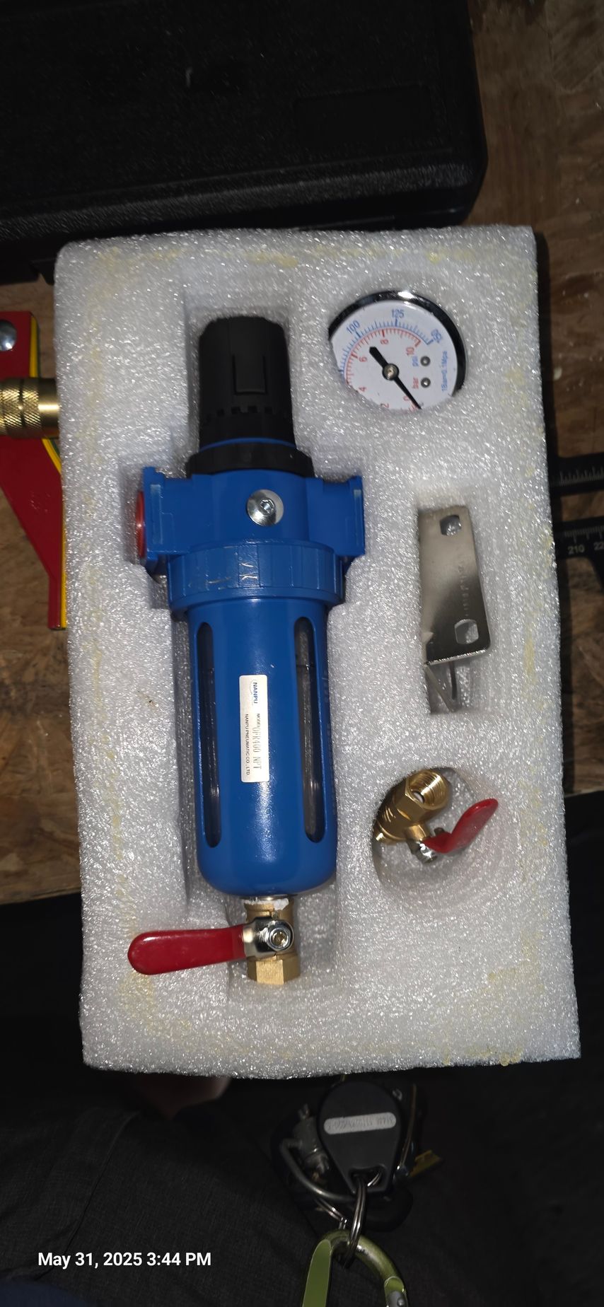 Blue air filter regulator, pressure gauge, bracket, and valve in foam packaging.
