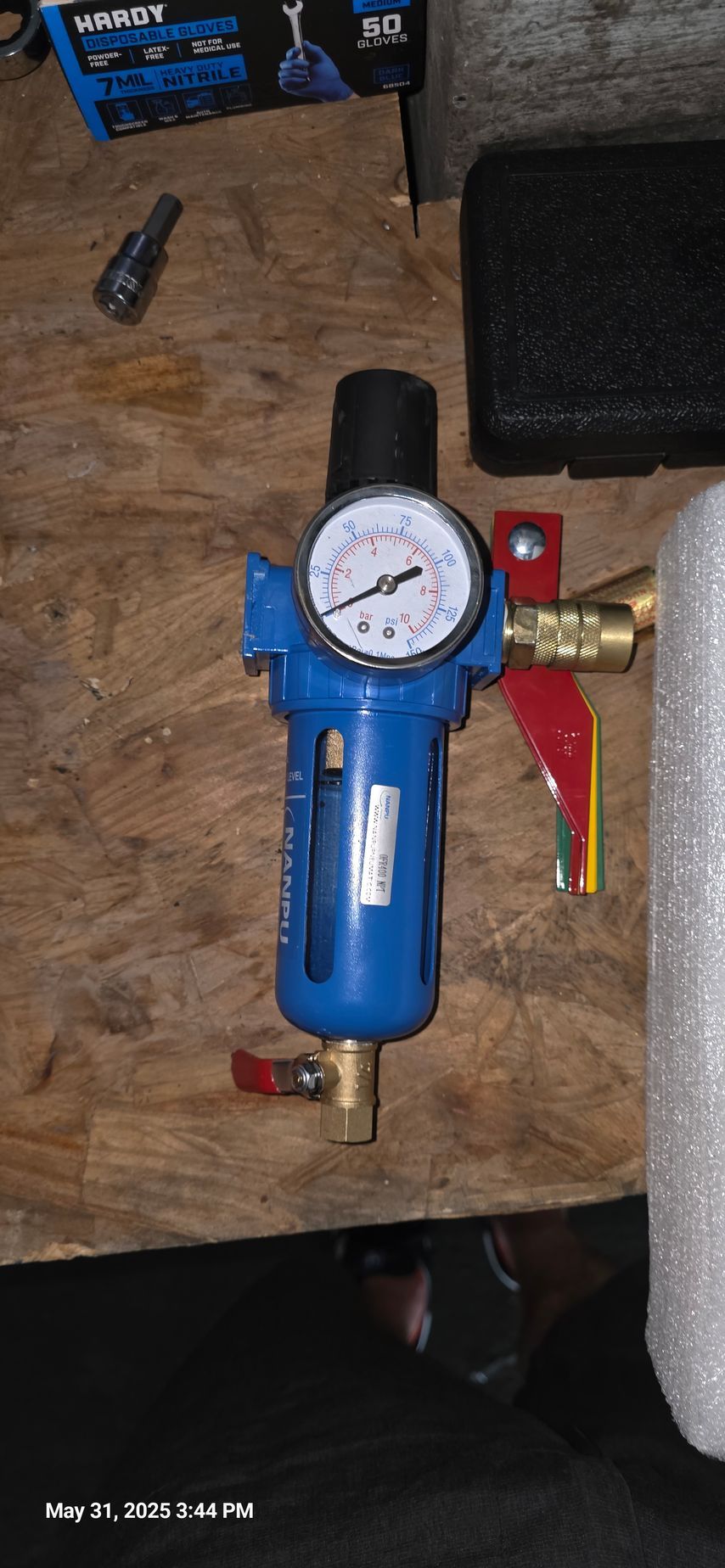 A blue air filter with a gauge and brass fittings rests on a wooden surface.