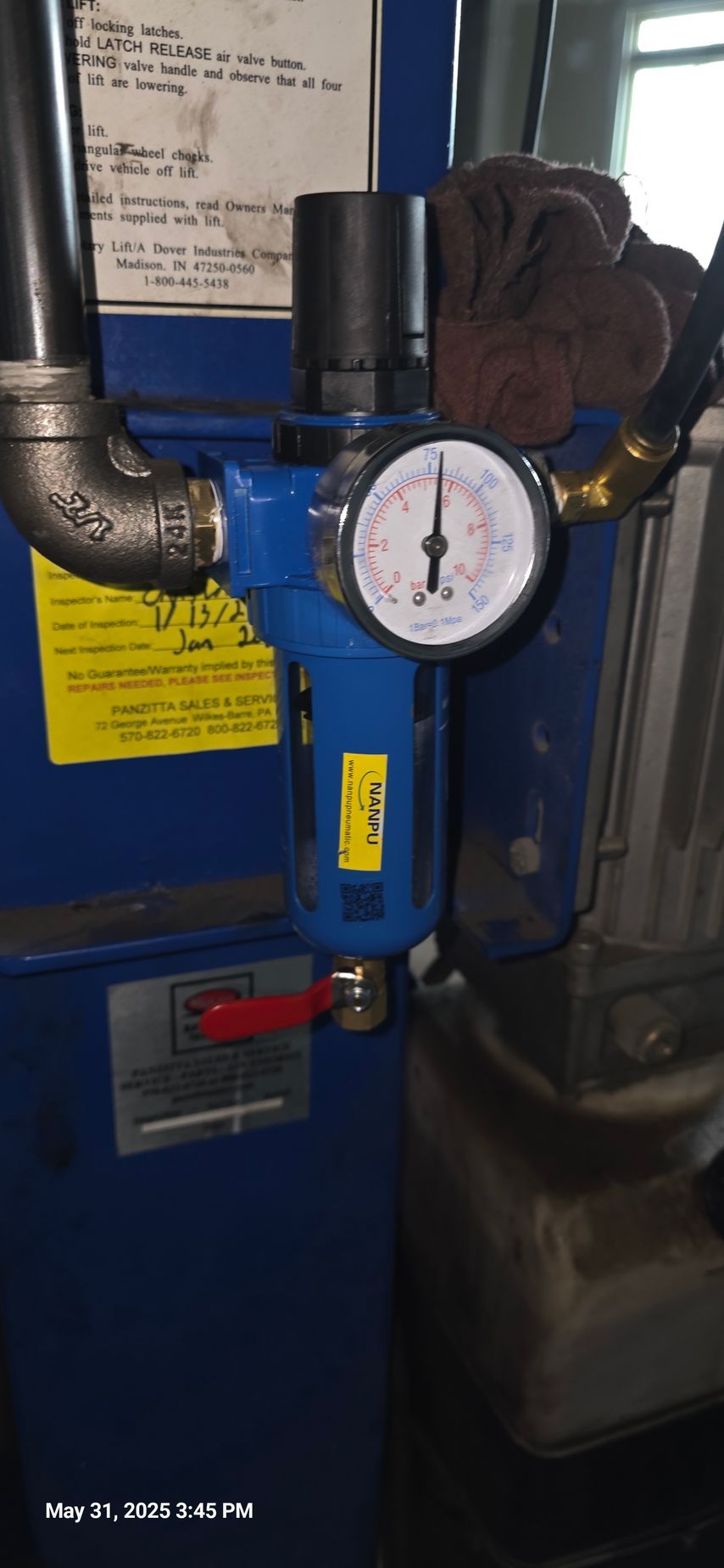 A blue air filter with a gauge, pipes, and a red lever attached to machinery.