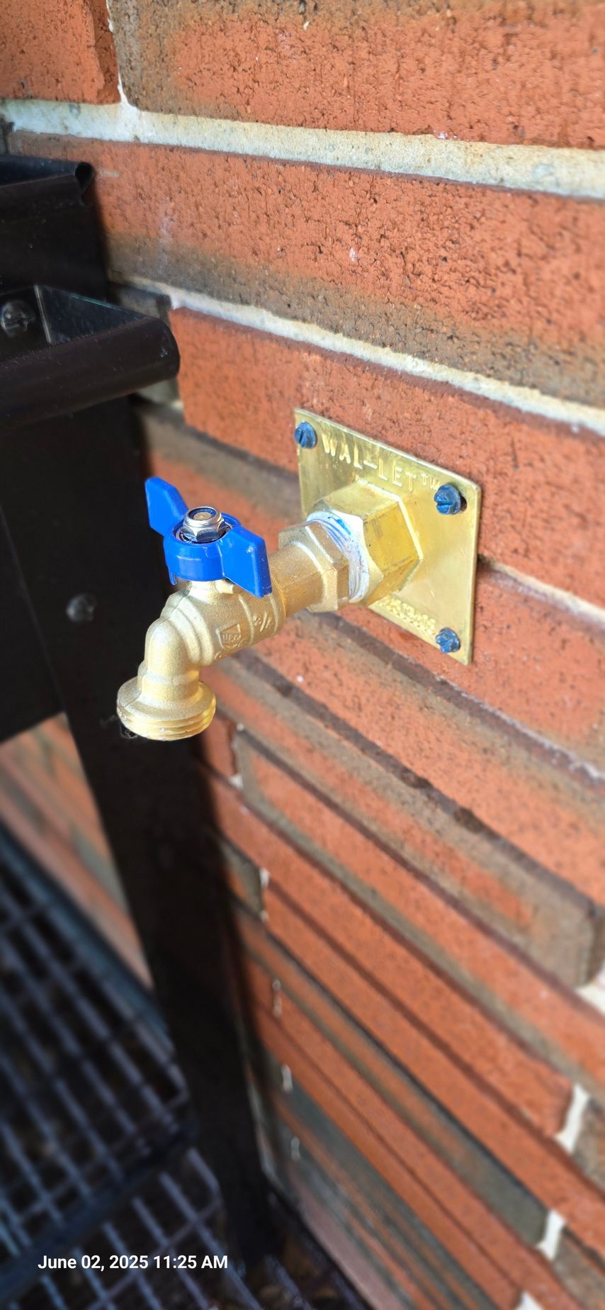 Brass spigot with blue handle on a brick wall.