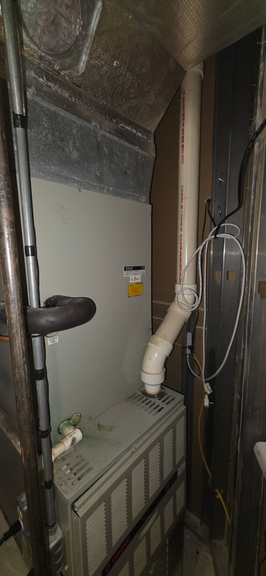 Furnace in a cramped space, with white PVC exhaust pipe.
