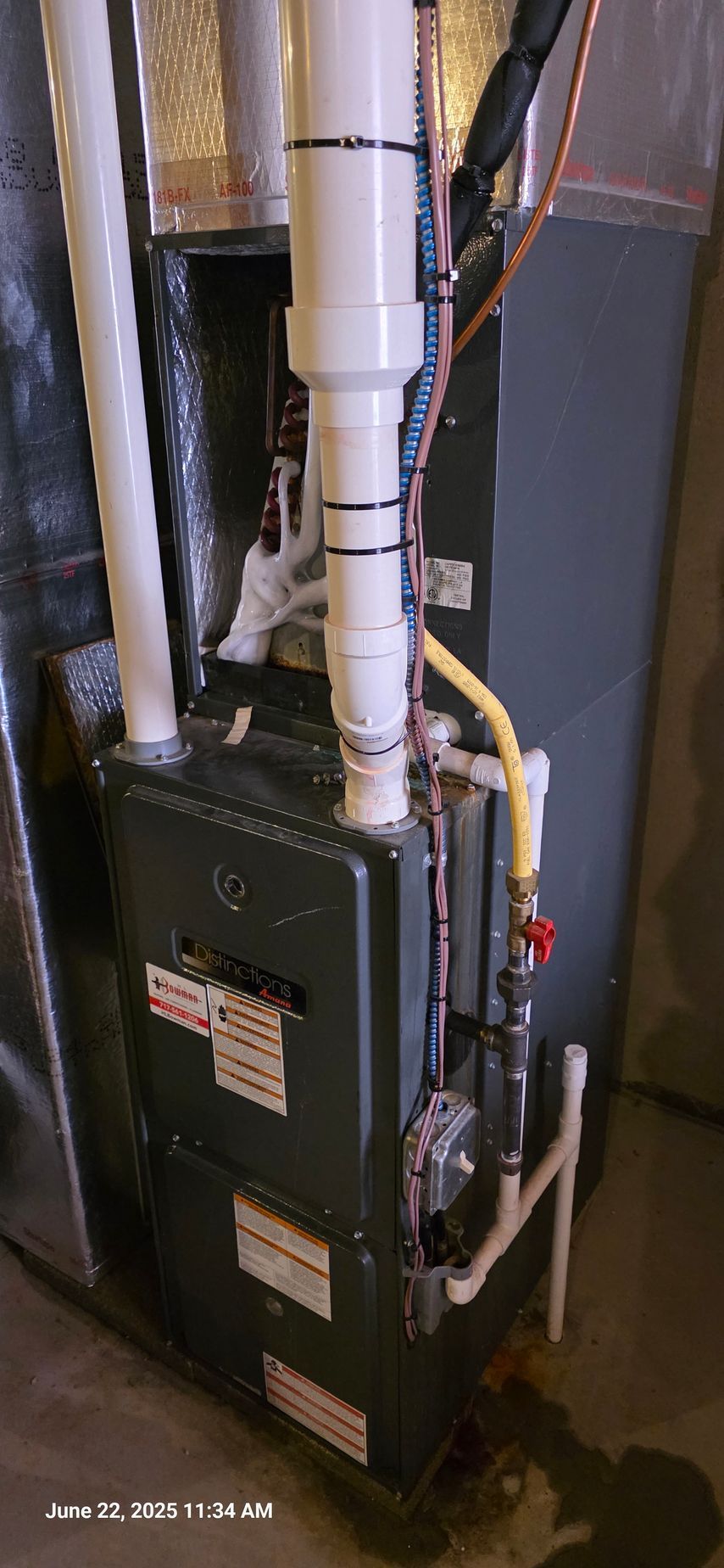 Furnace with white PVC pipes, gas line, and control panel. Gray, indoor setting.