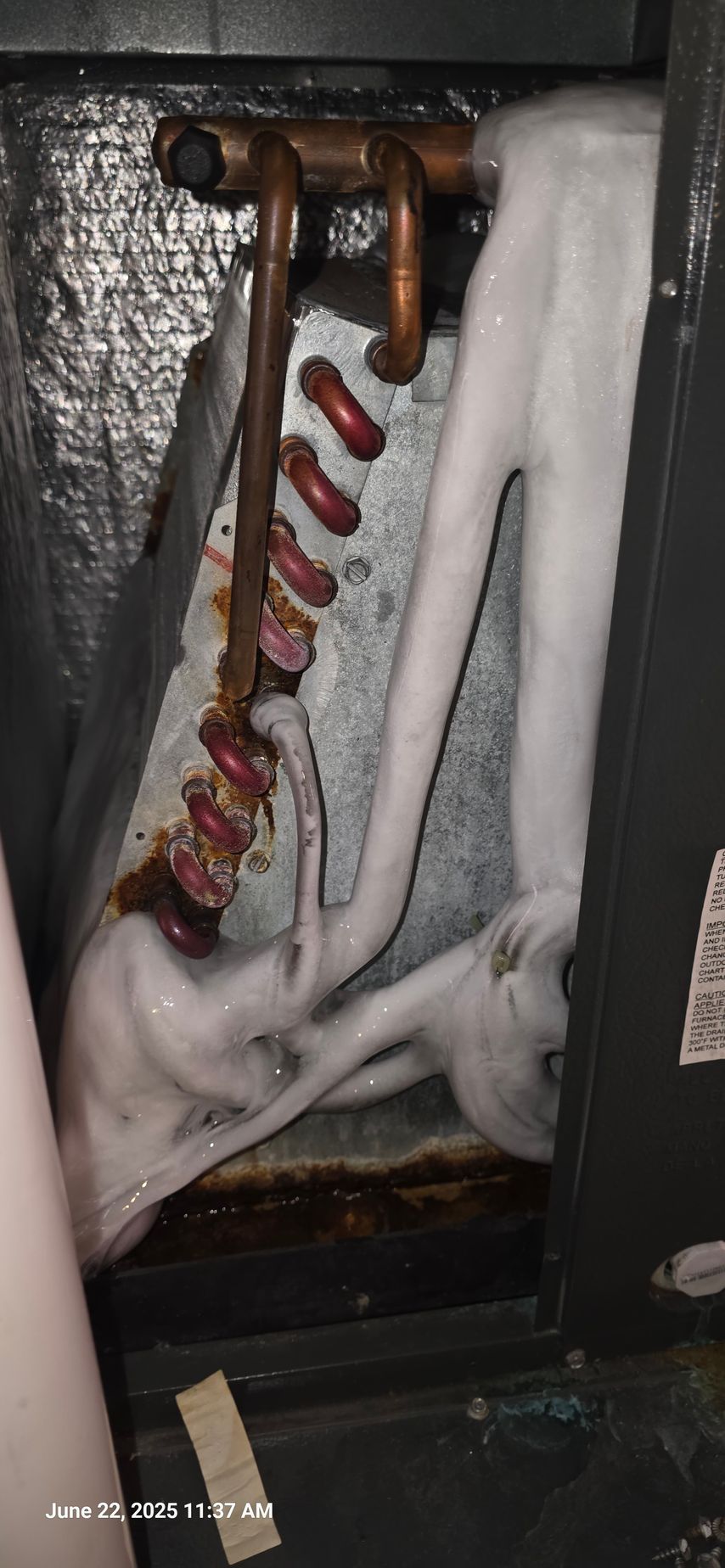 An air conditioning unit's evaporator coil is covered in ice. Copper pipes and the unit's interior are visible.