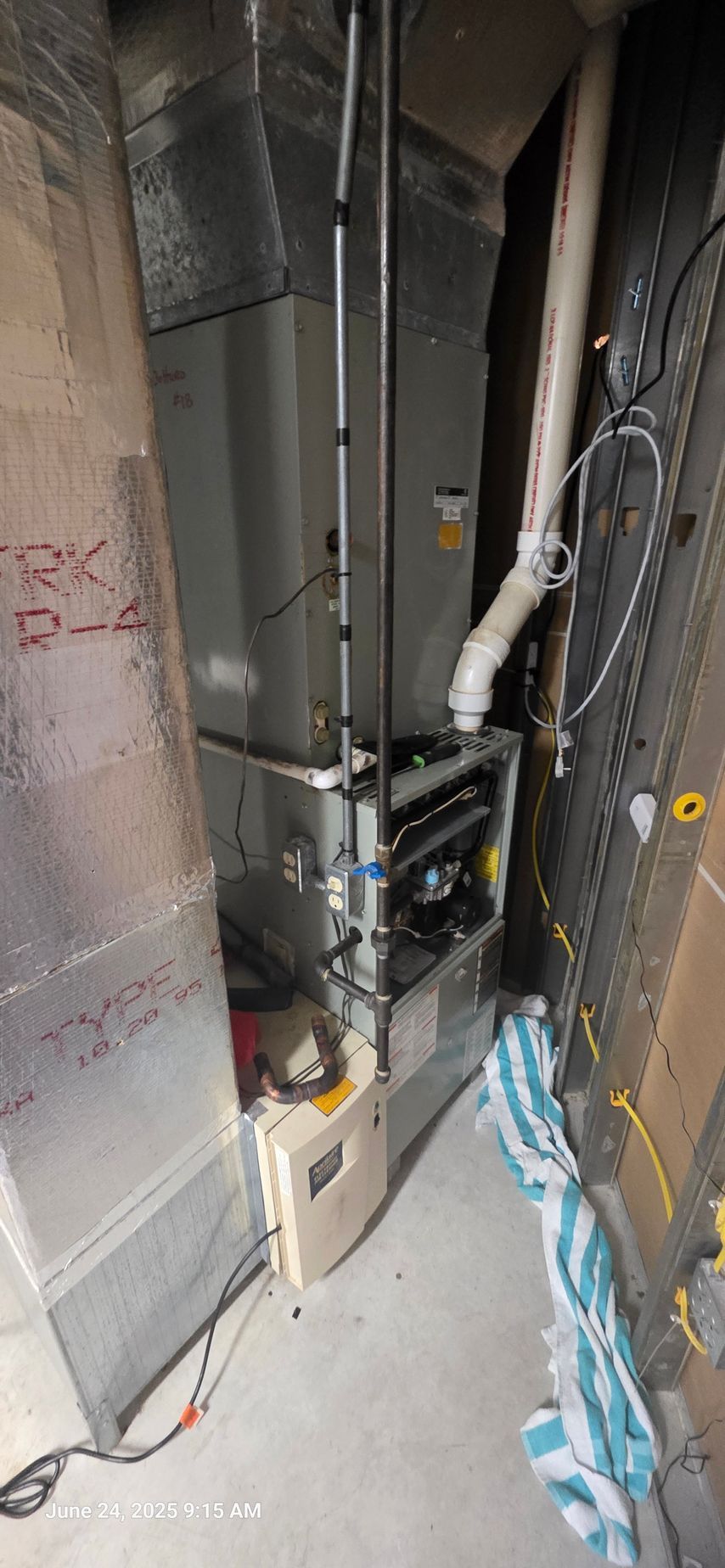 A furnace in a utility room with metal ductwork, pipes, and electrical wiring.