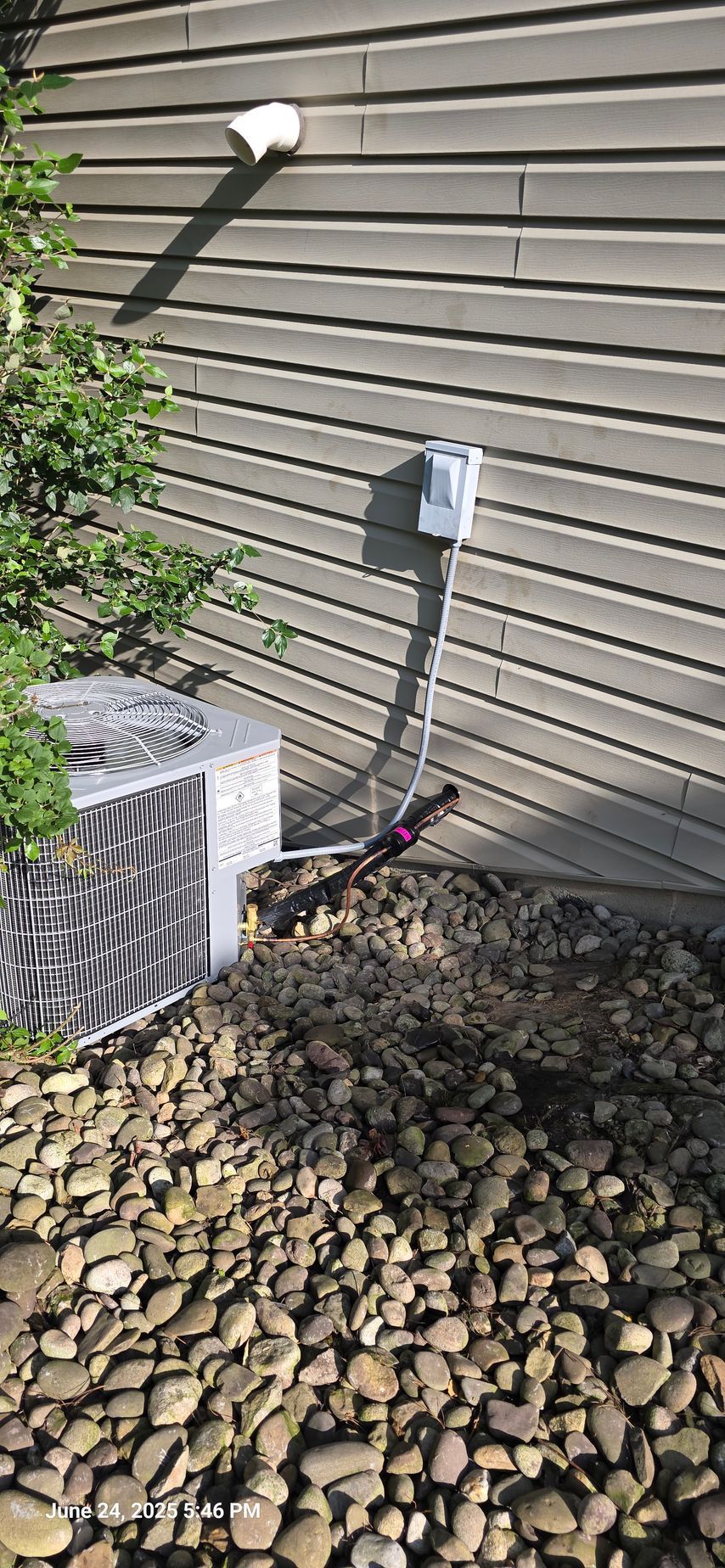 An air conditioning unit next to a house with gravel ground covering.