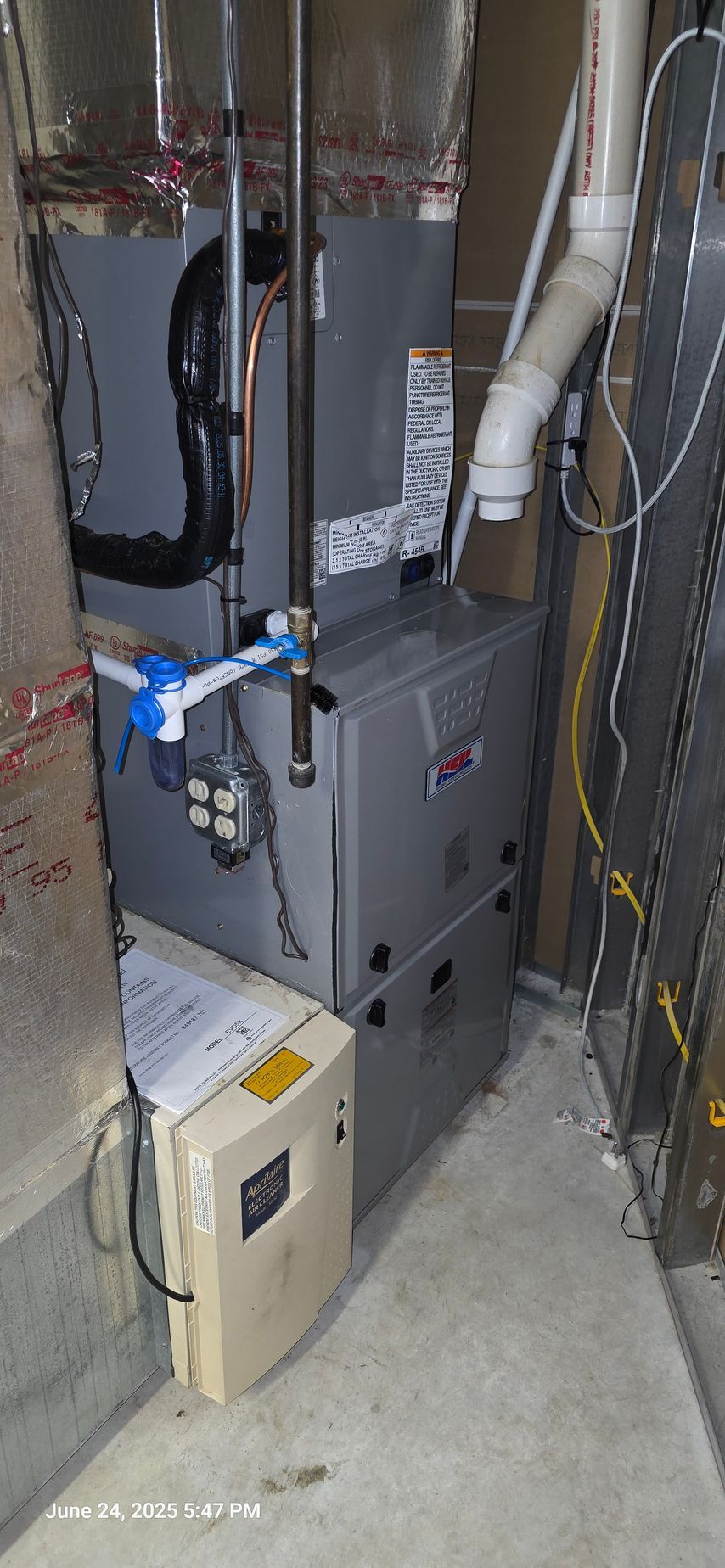 A furnace and attached electrical box in a utility room. Gray metal and white pipes.