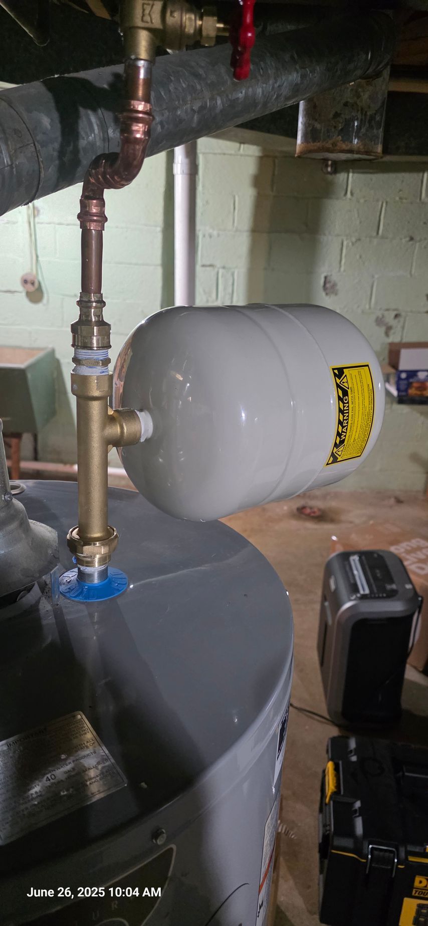 Water heater with expansion tank and copper pipes in a basement.