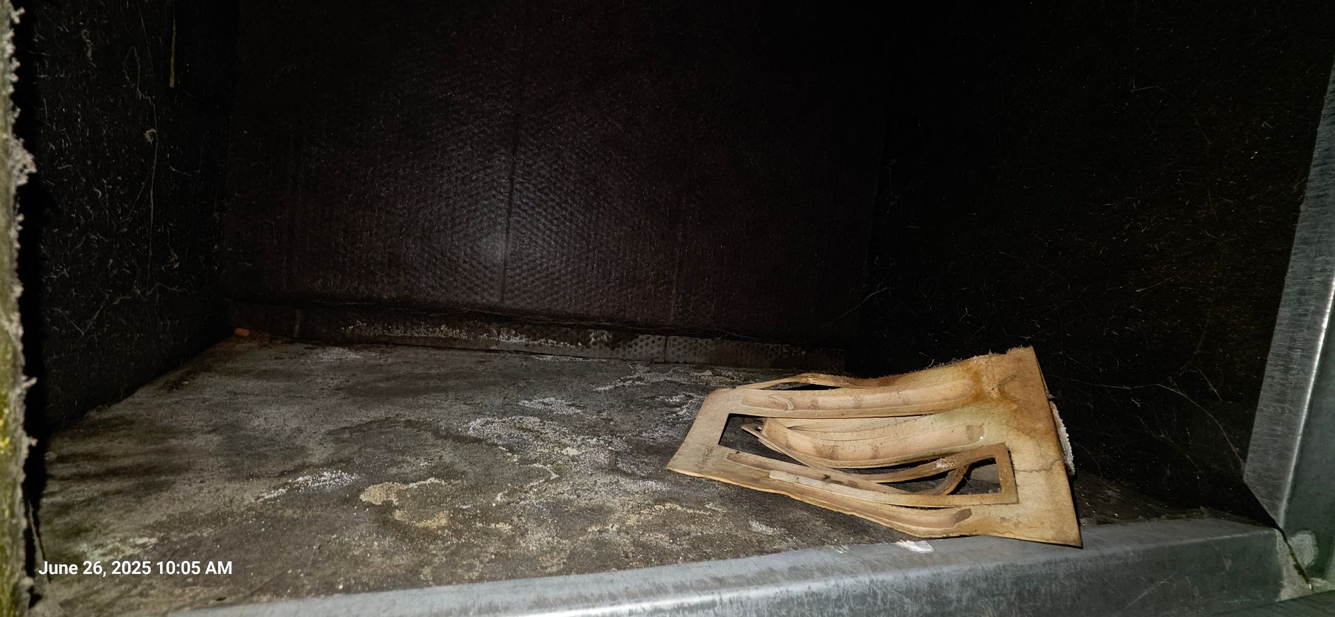Inside of a dark, dusty cabinet. A light-colored, broken object sits on the bottom.