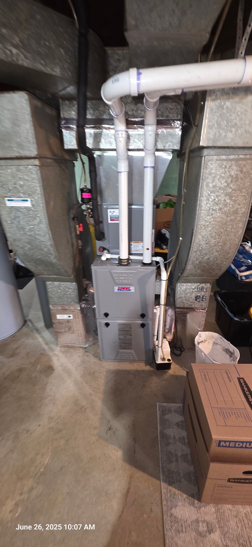 Furnace in a basement with metal ductwork and white PVC pipes. A cardboard box is in the foreground.