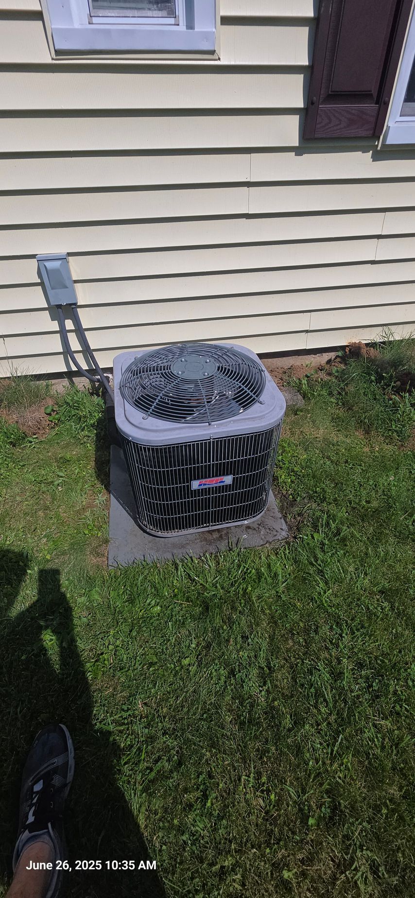 Air conditioning unit outside a yellow house. The unit sits on a concrete pad, surrounded by grass.
