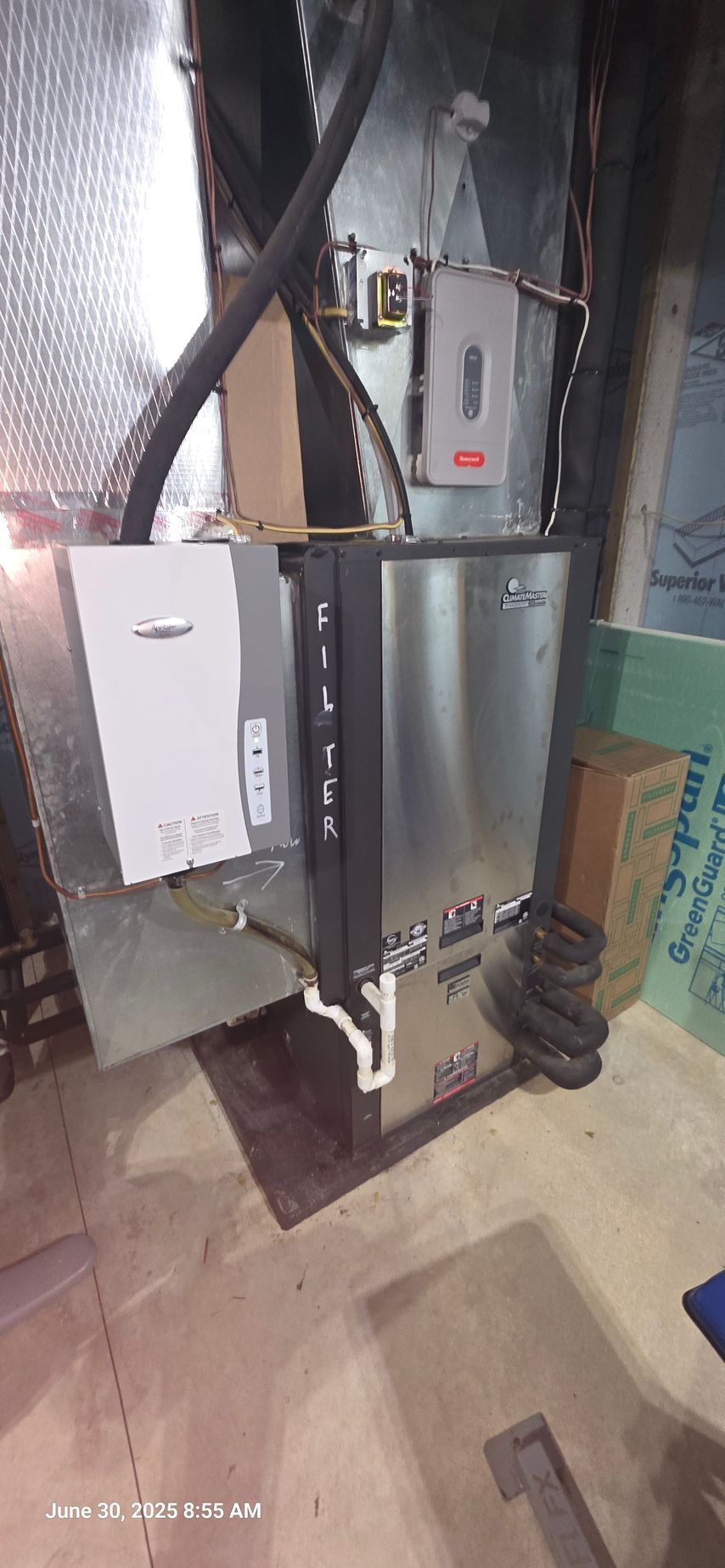 Furnace and related equipment in a basement. Silver metal and black components. PVC drain pipe.