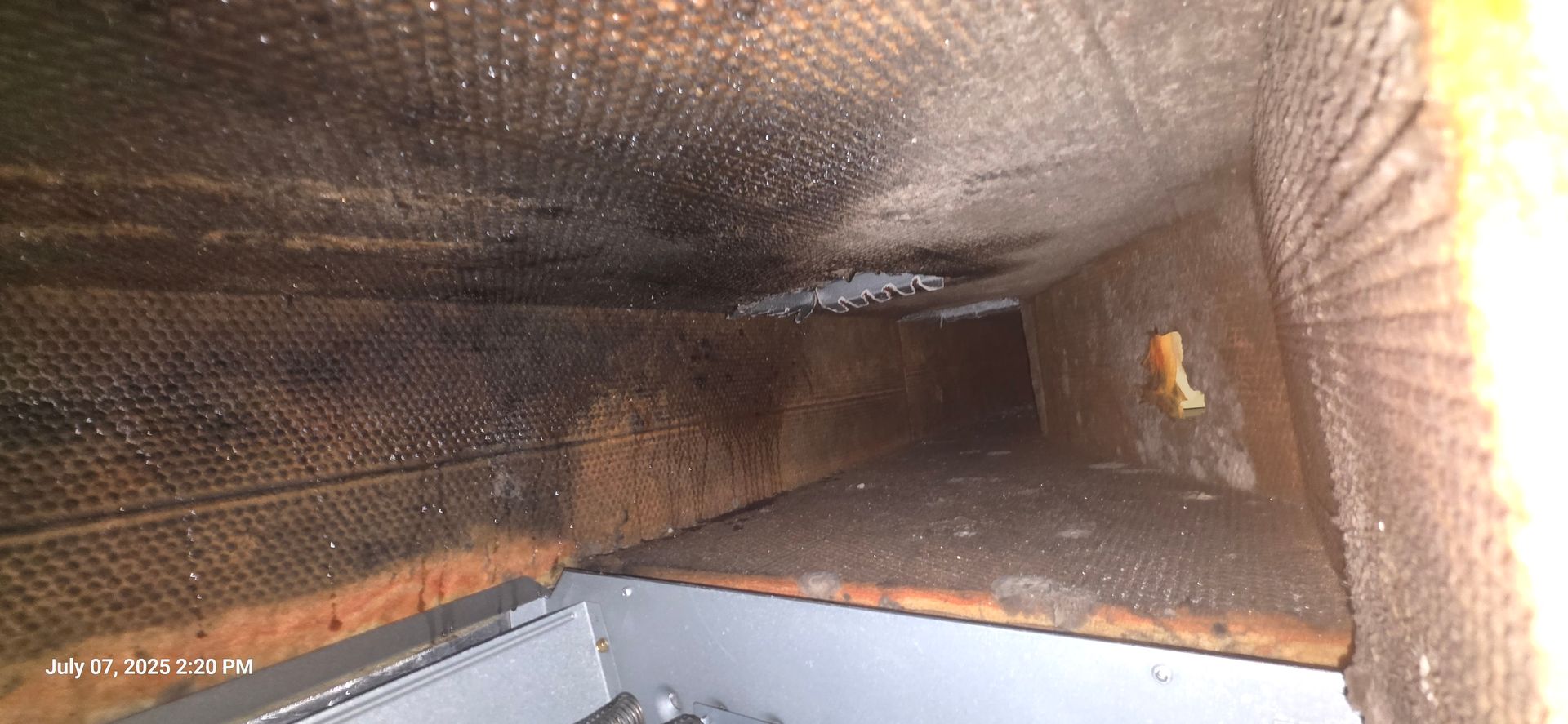 Interior view of a dirty air duct with dark residue and debris.