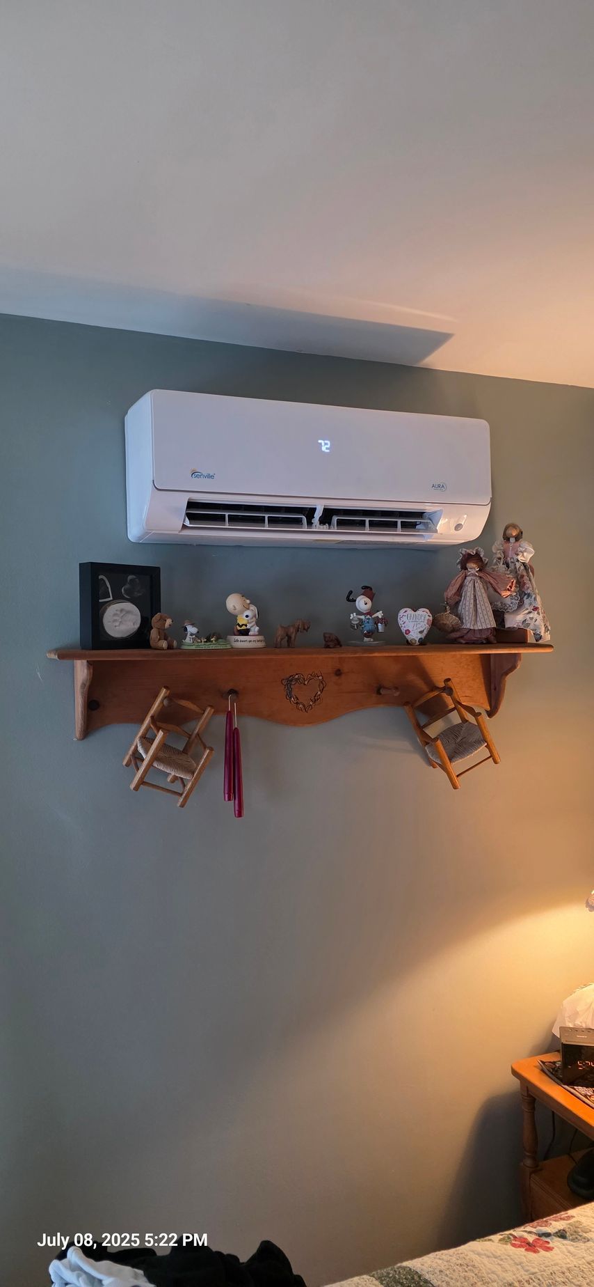 A white air conditioner above a shelf with decorations against a green wall.