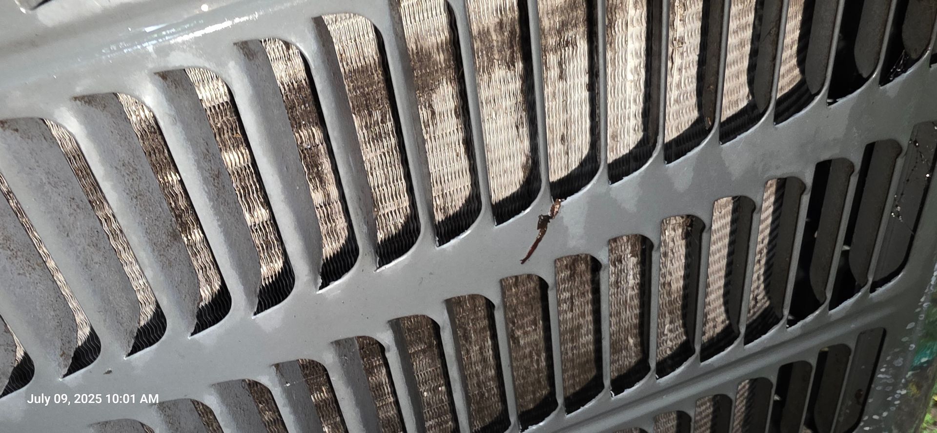 Close-up view of a dirty air conditioner grill with slots, showing a buildup of dirt and debris.