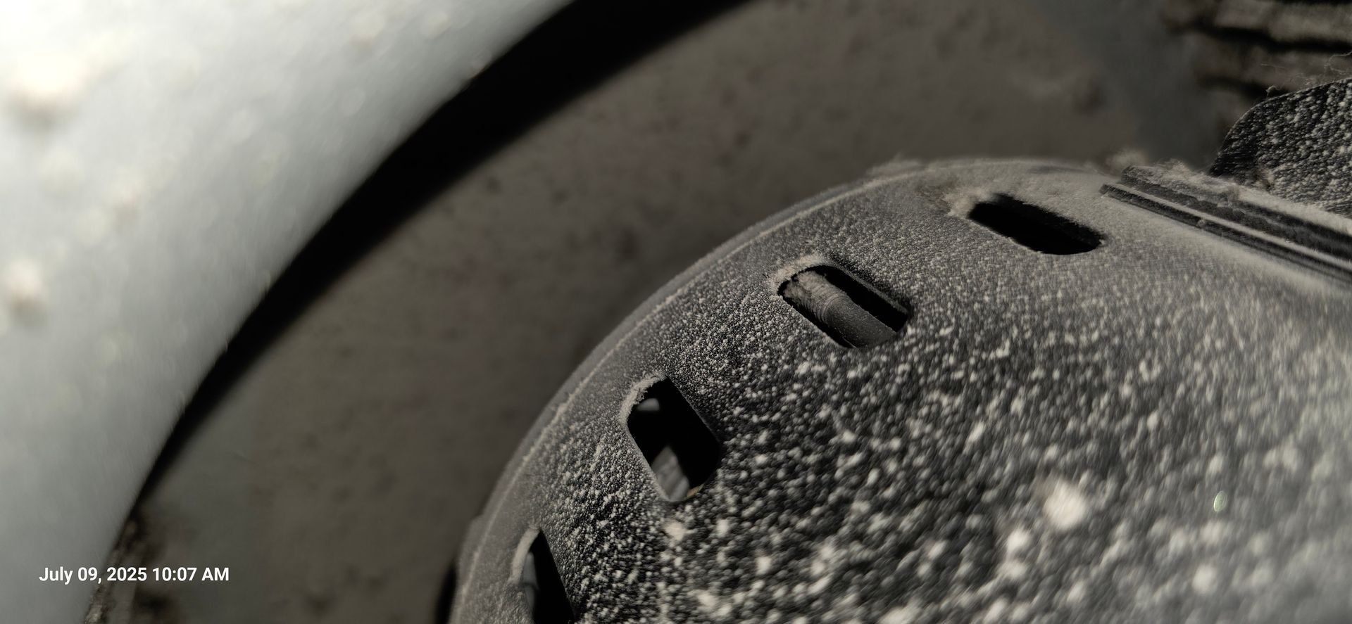 Close-up of a dusty, perforated metal object, possibly part of machinery, with a curved white surface on the left.