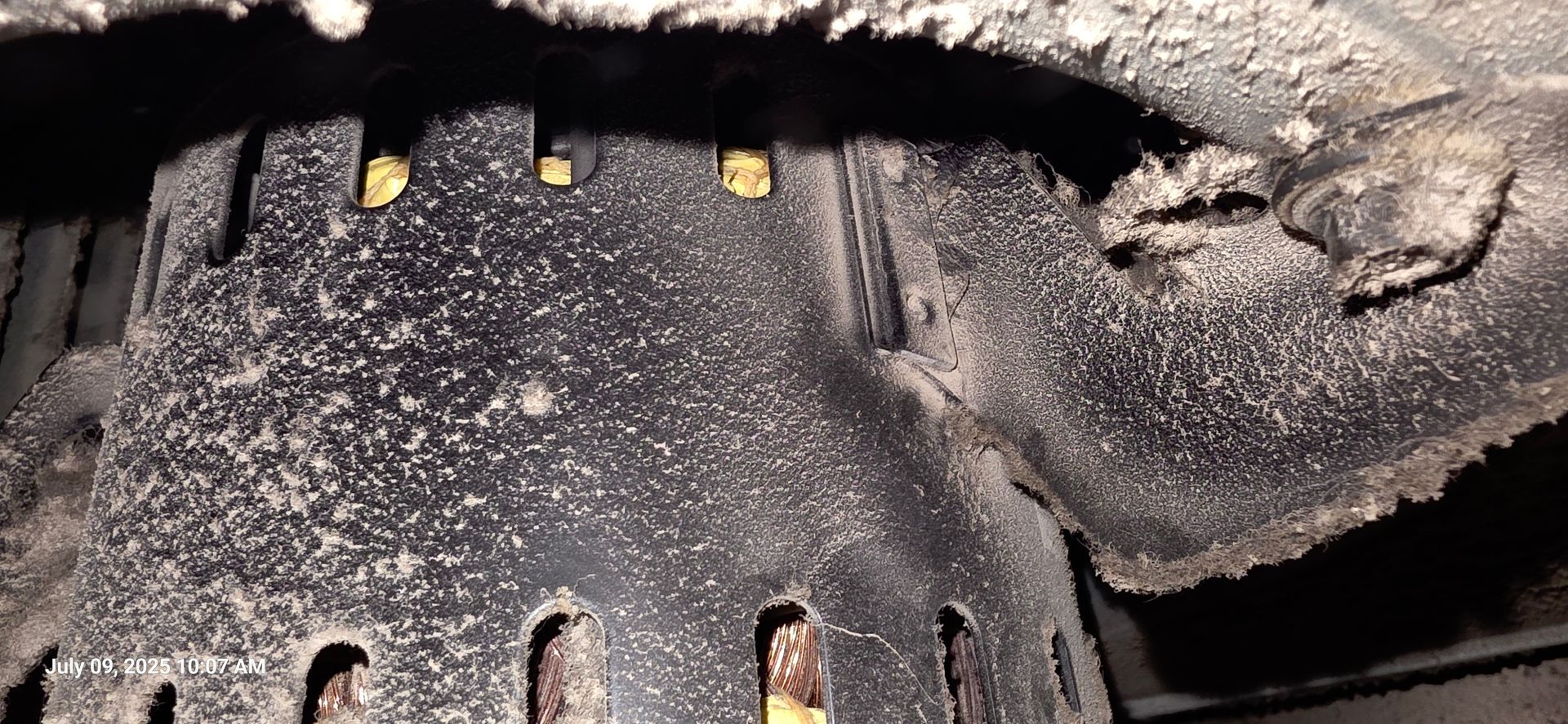 Close-up of a dusty, dark metal object with several openings and some gold-colored pieces.