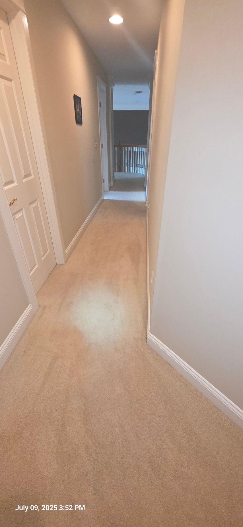 Narrow beige carpeted hallway with doors and recessed lighting.