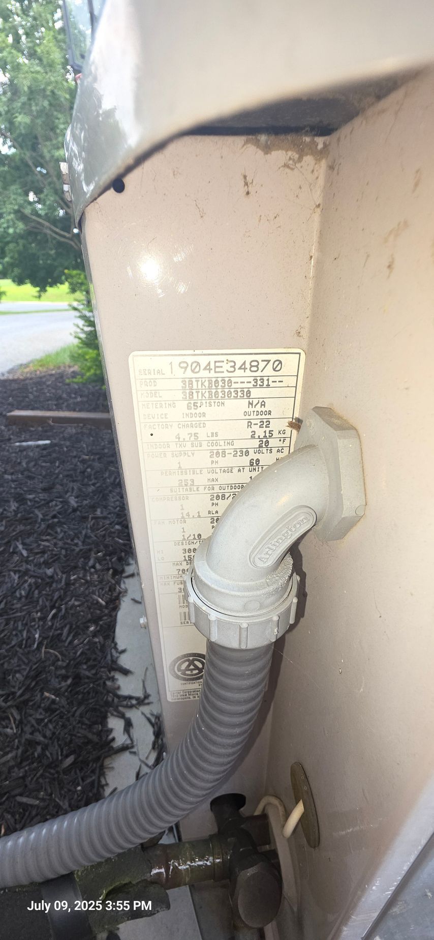 Close-up of an air conditioning unit's side. Includes a label with text and wiring conduit.