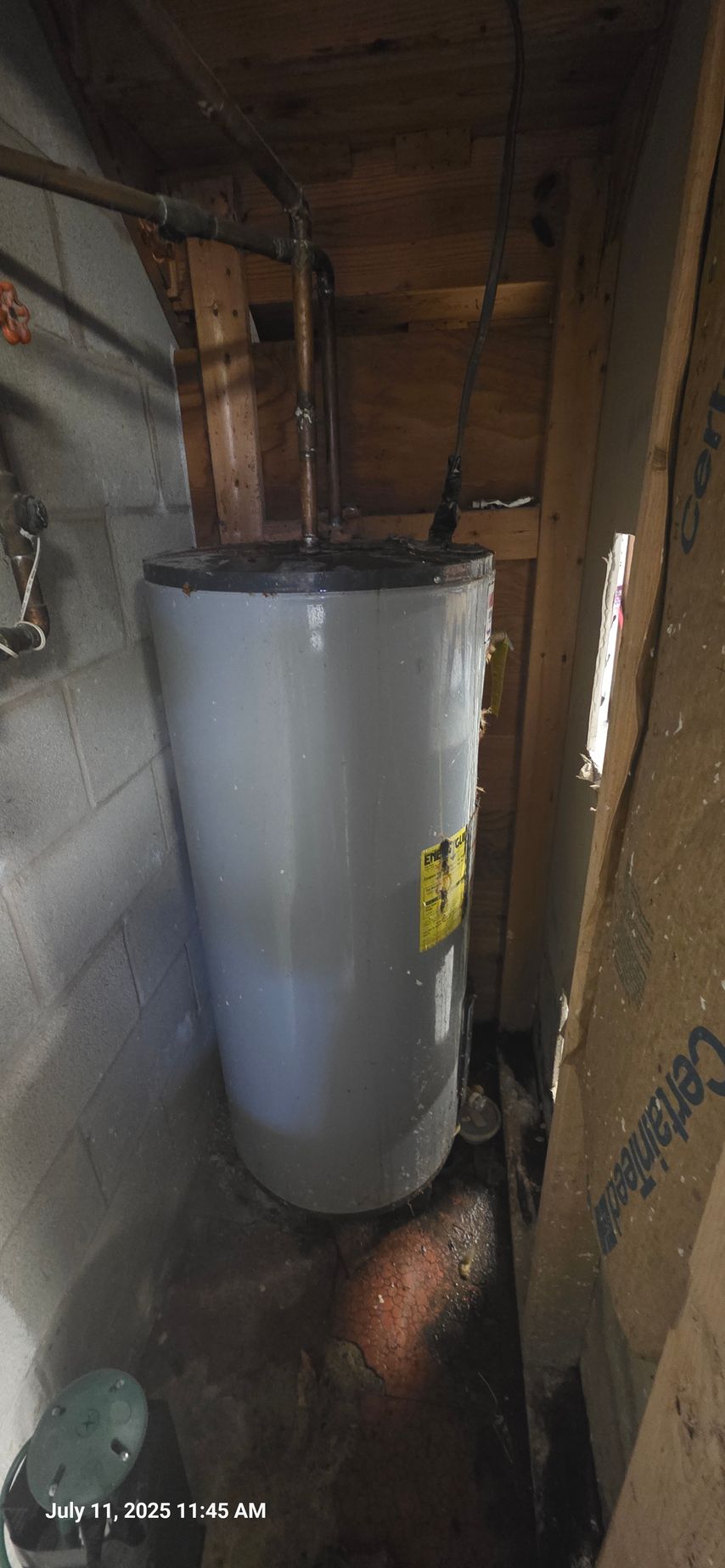 A water heater sits in a tight space. Water leaks from it, and there is water on the floor.