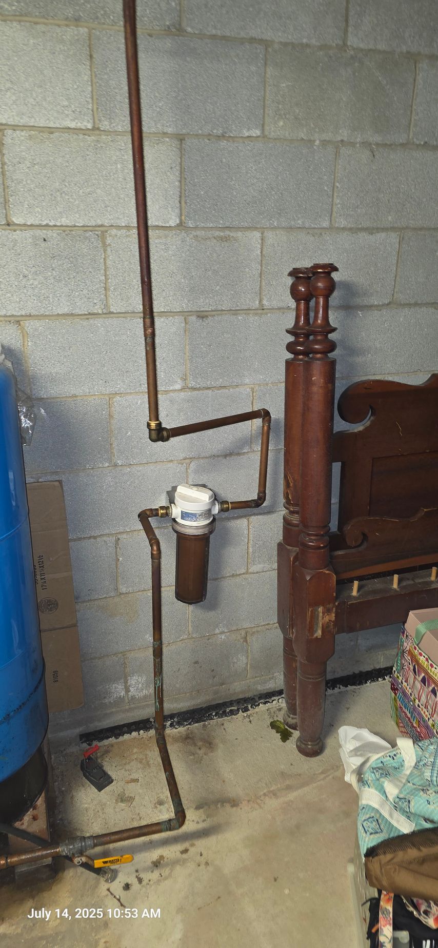 Copper pipes connected to a water filter and a large blue tank against a cinder block wall.