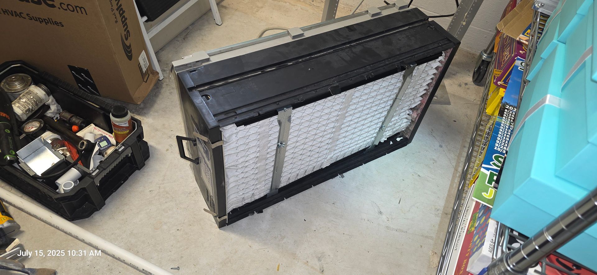Black rectangular light fixture, possibly for photography, on a concrete floor with a toolbox and a storage container nearby.