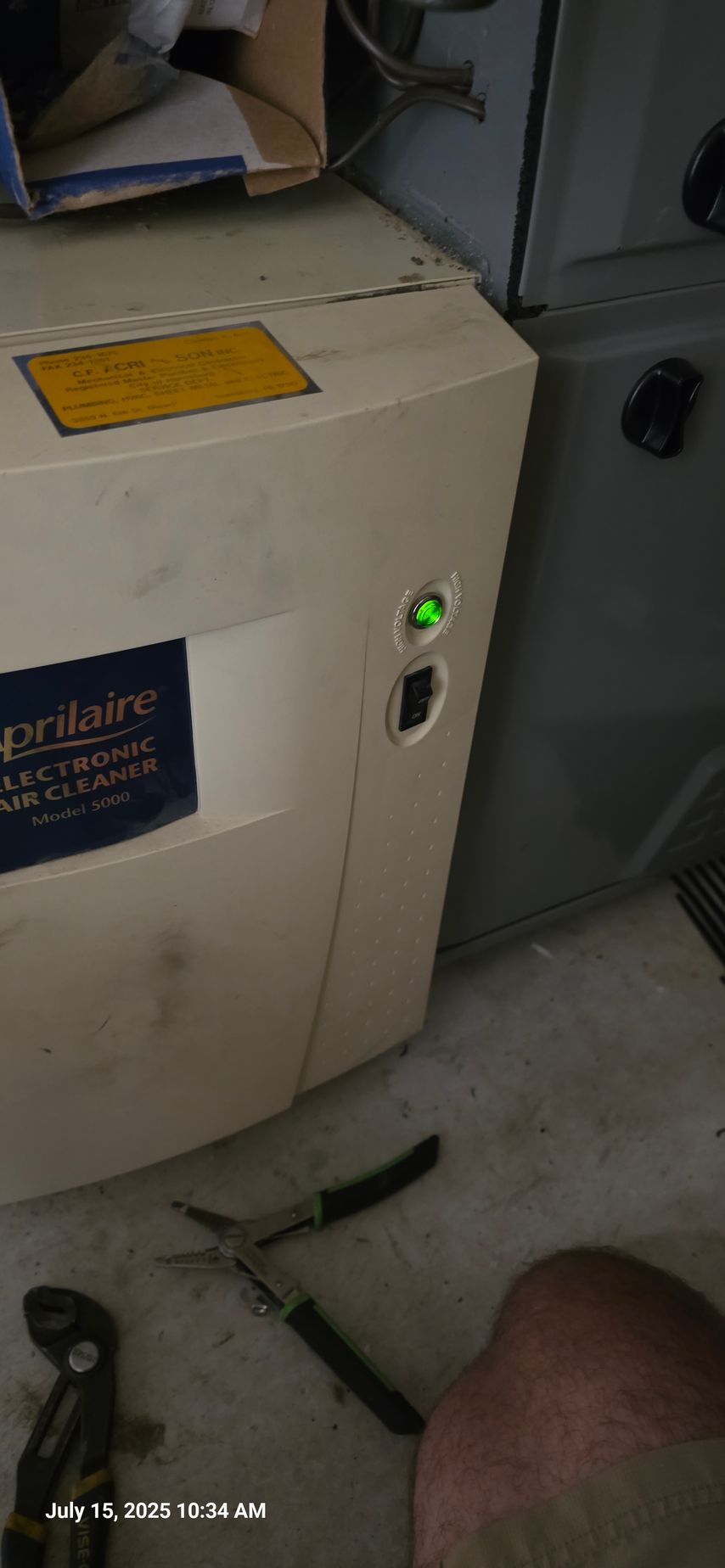 An air filtration system with a green light on, next to another appliance. Tools and a leg are in the foreground.