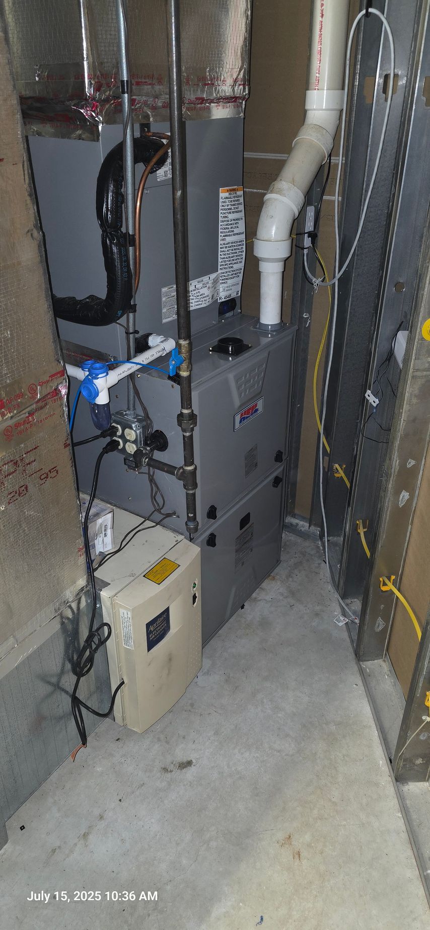 Furnace in a basement setting with ductwork and a water heater. Grey and white components on a concrete floor.