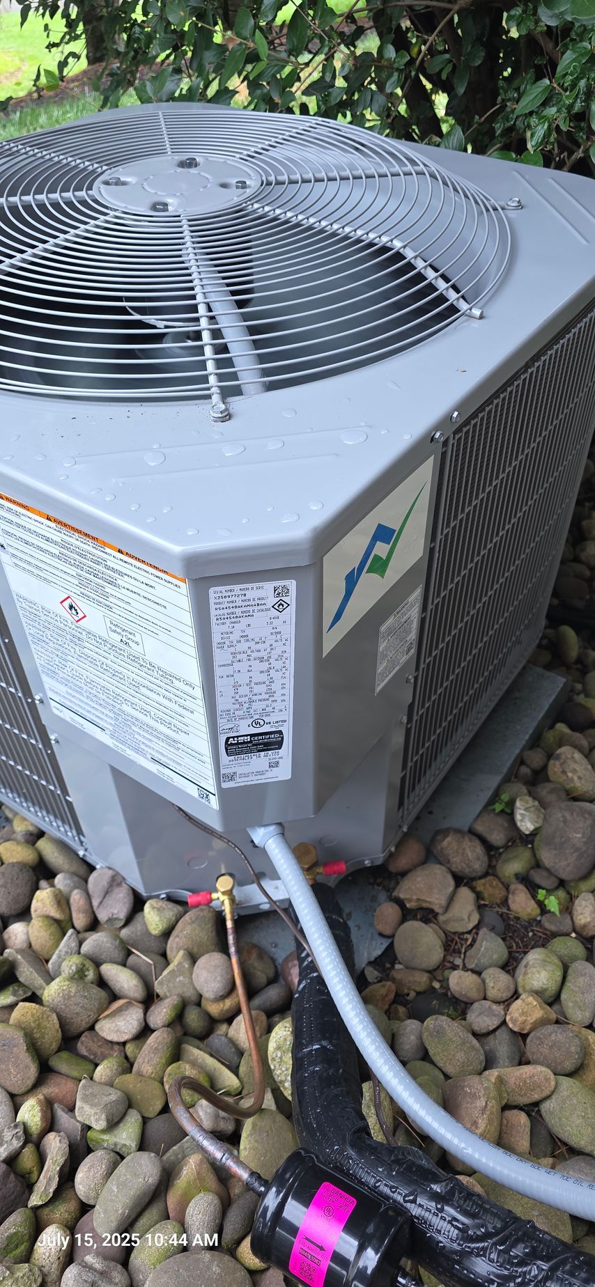 An air conditioning unit sits on a bed of rocks. It has a fan on top.