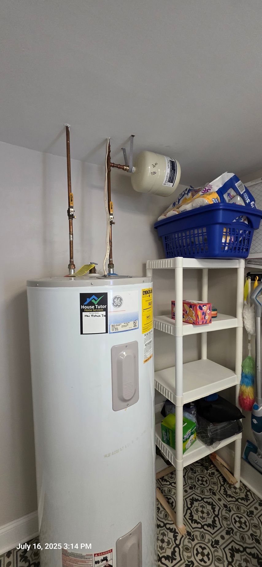 A white water heater in a utility room with copper pipes and a small shelf unit with storage.