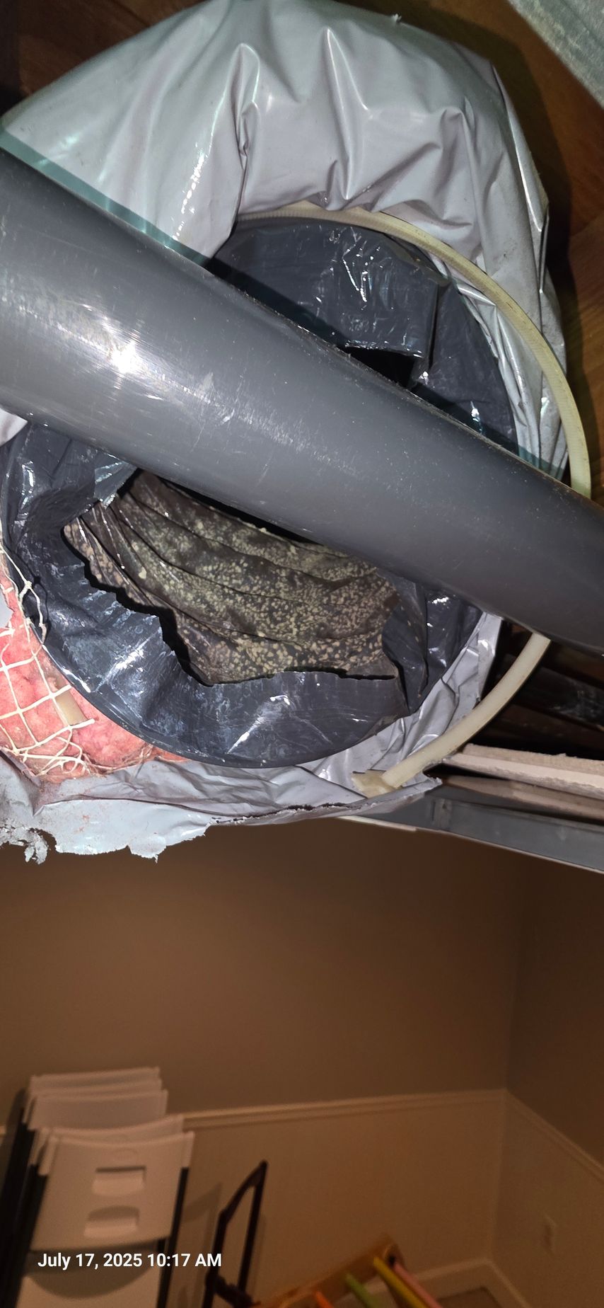 Inside a duct: gray pipe, black plastic bag holding gray material, surrounded by insulation.