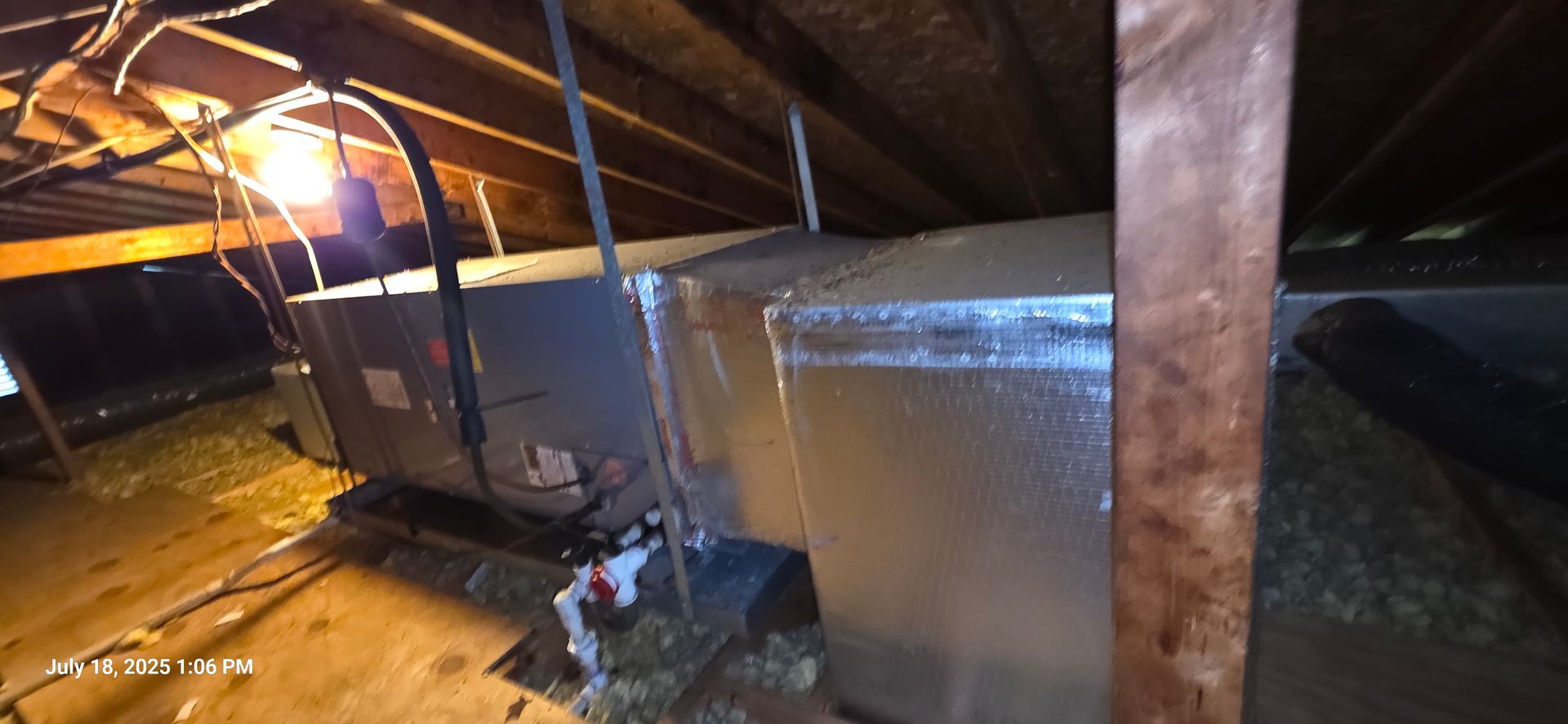 An HVAC unit and ductwork in an attic, with wooden beams and insulation.