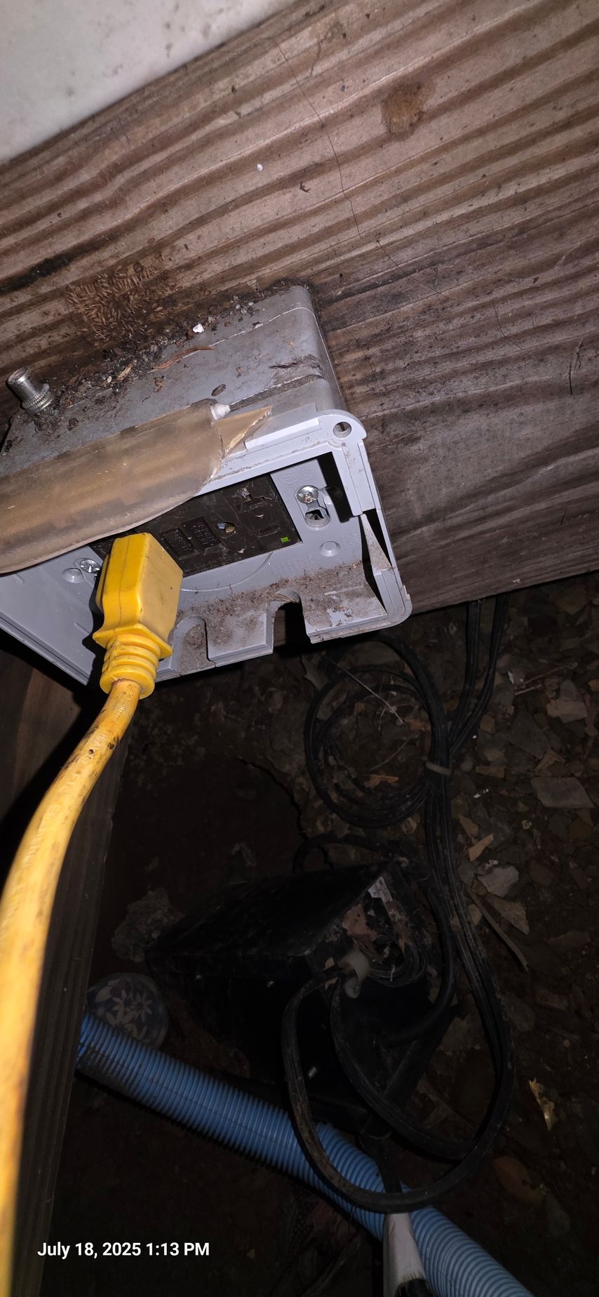 A yellow power cord plugged into an electrical box, mounted on wooden boards, in a dark space.