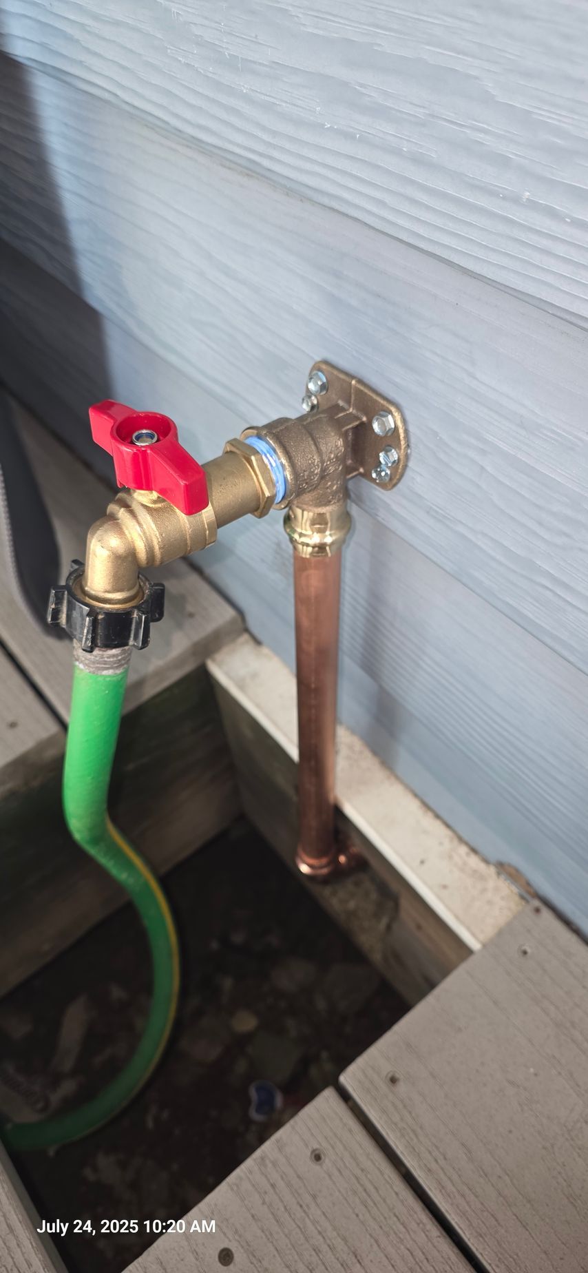 Outdoor faucet with a red handle and green hose attached.  Copper pipe leads to a wall.