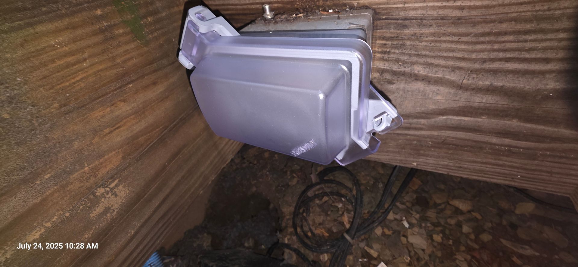 A translucent plastic container is attached to wooden planks. Some electrical wiring is visible in the lower part of the photo.