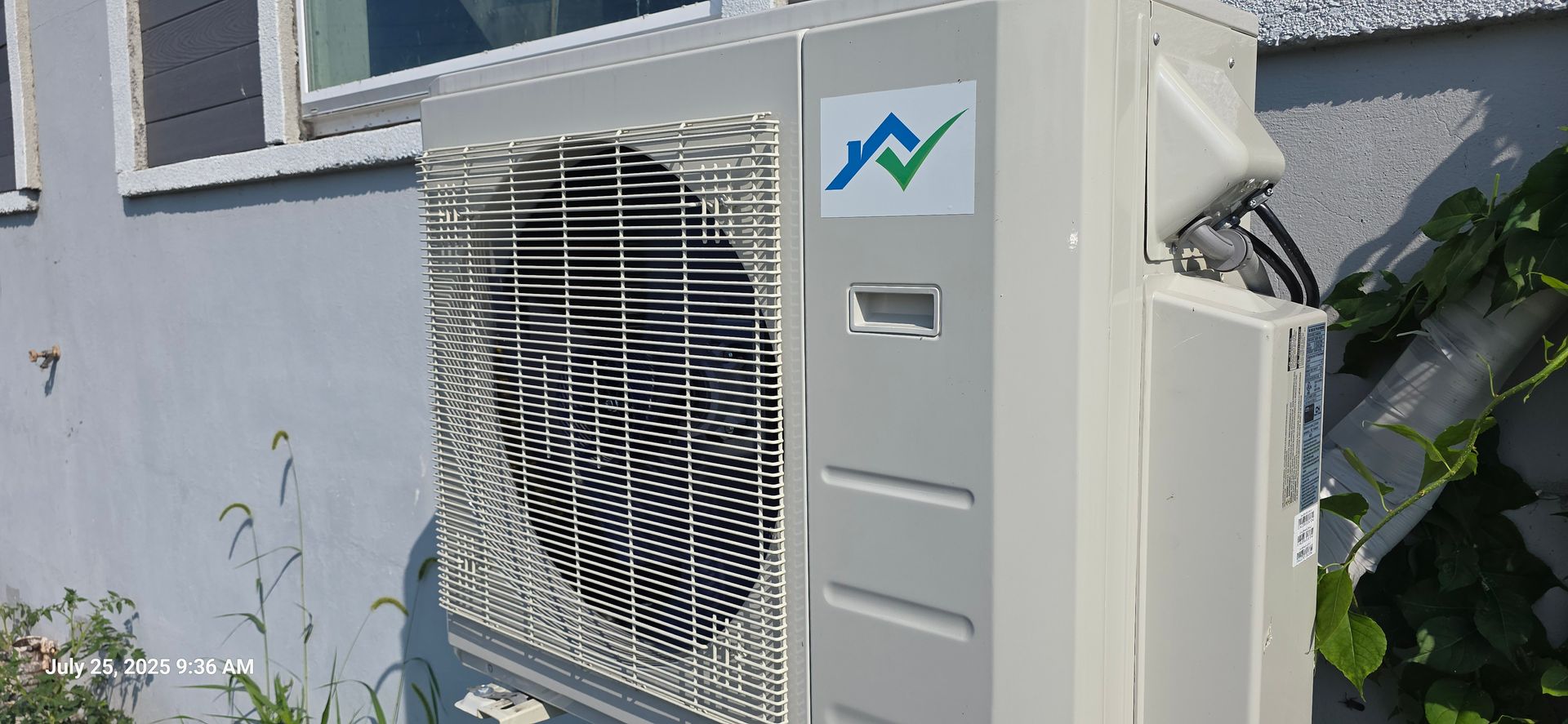 An air conditioning unit is mounted outside against a light blue wall, with green vines creeping up the side.