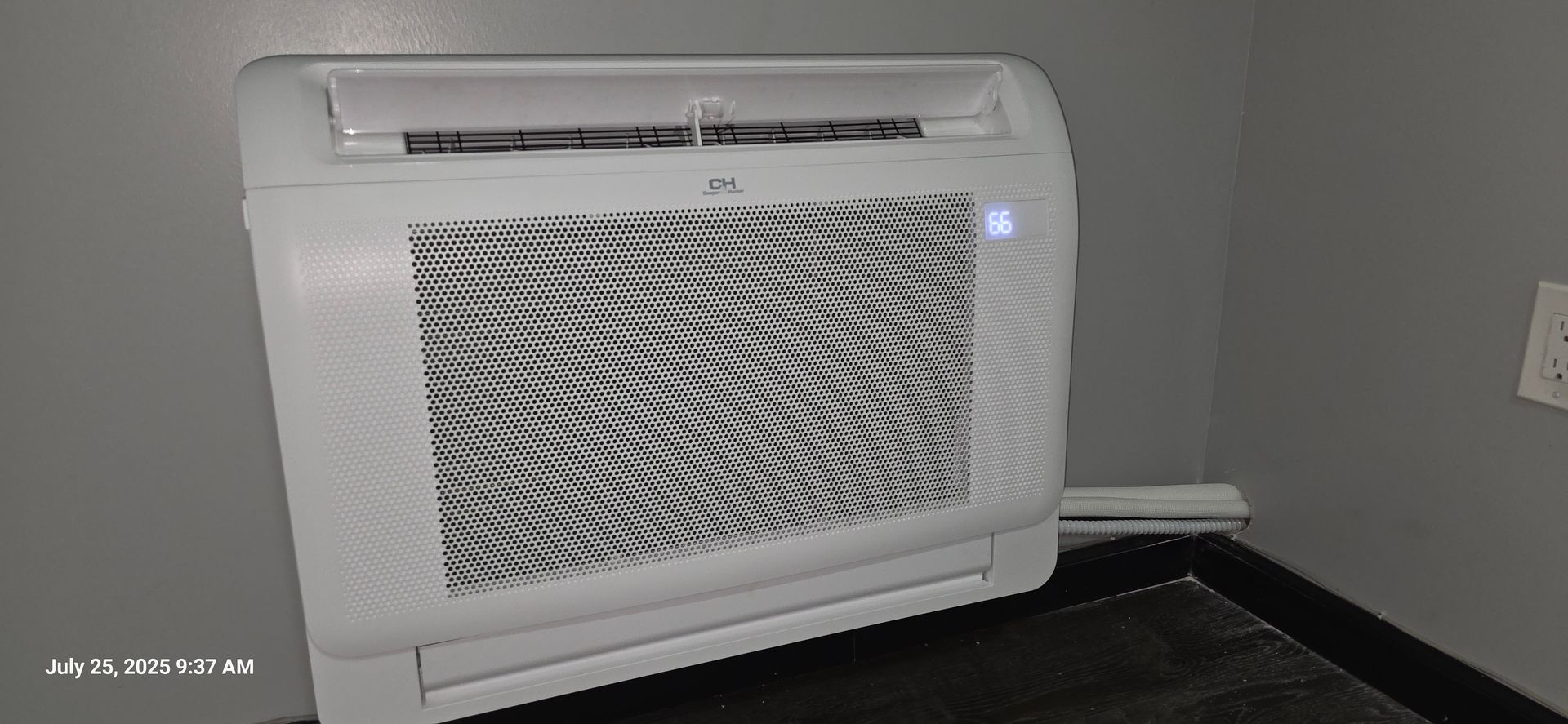 White air conditioner unit mounted on a dark surface in a room with gray walls.