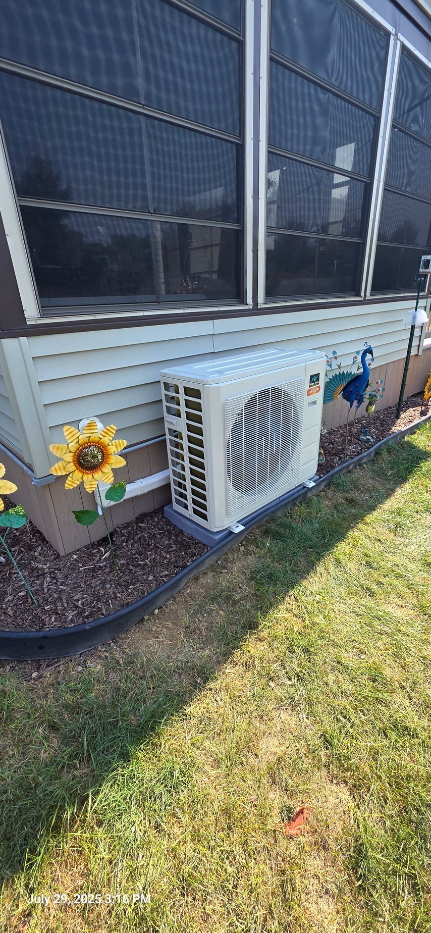 An air conditioning unit on a concrete pad near a building with windows and siding, with yard.