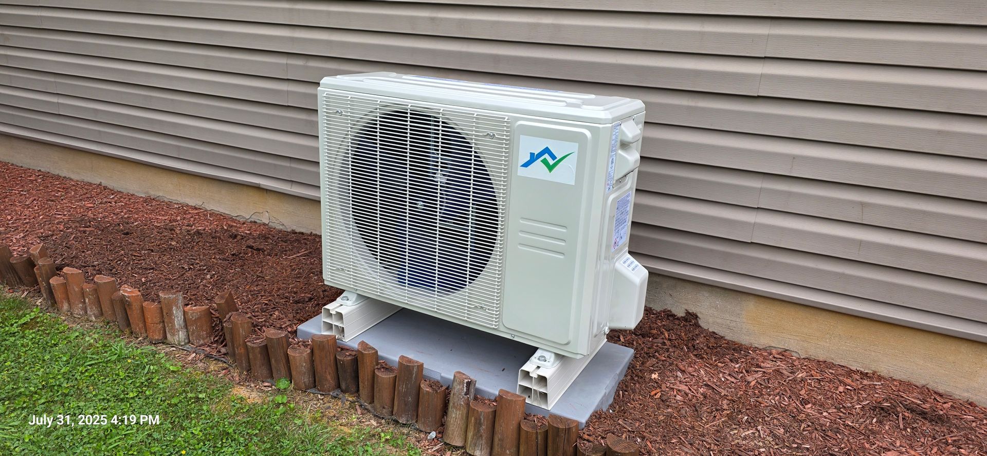 Air conditioner unit next to a house with mulch and a brick border.