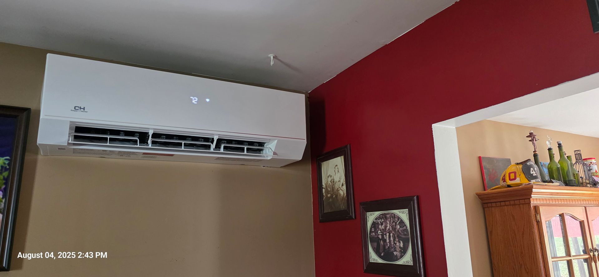 White wall-mounted air conditioner on beige wall. Red wall to the right with two framed pictures.