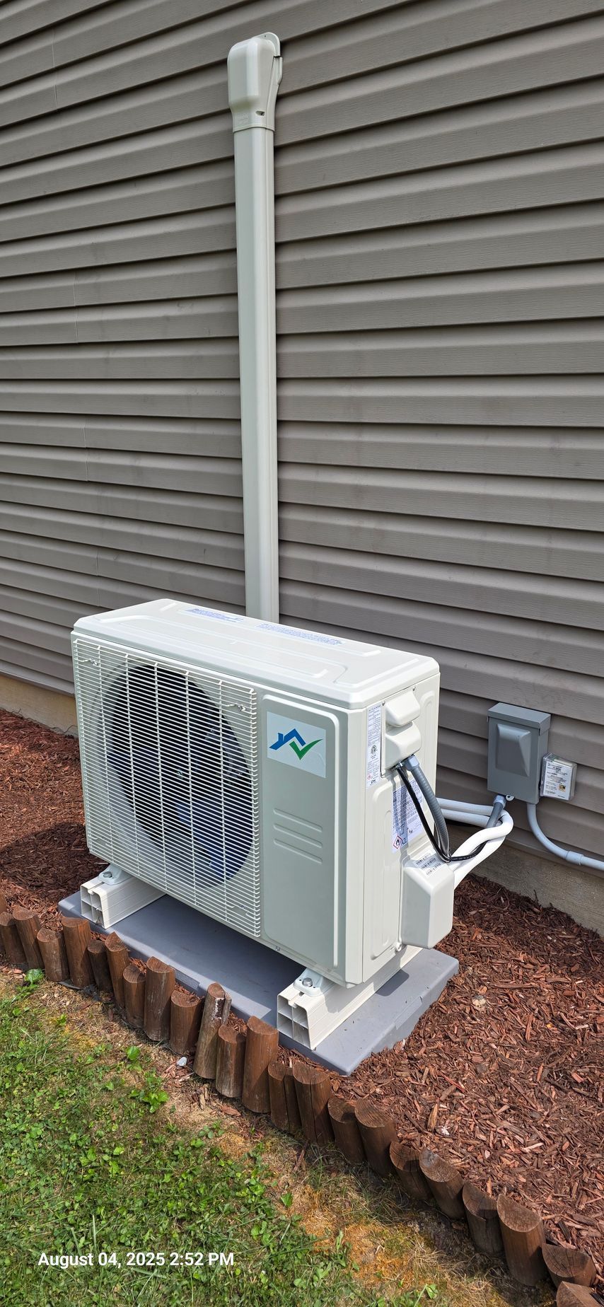 Outdoor air conditioning unit mounted on a concrete base next to a house with gray siding.