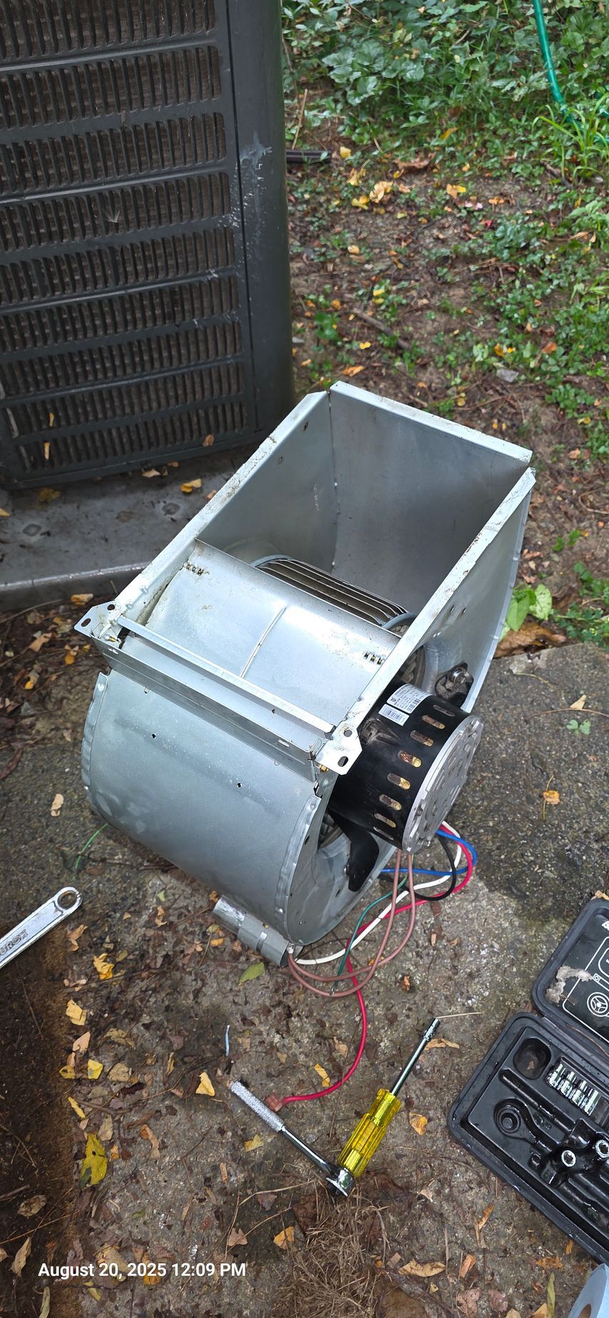Air conditioner fan motor removed from unit, on the ground near tools.